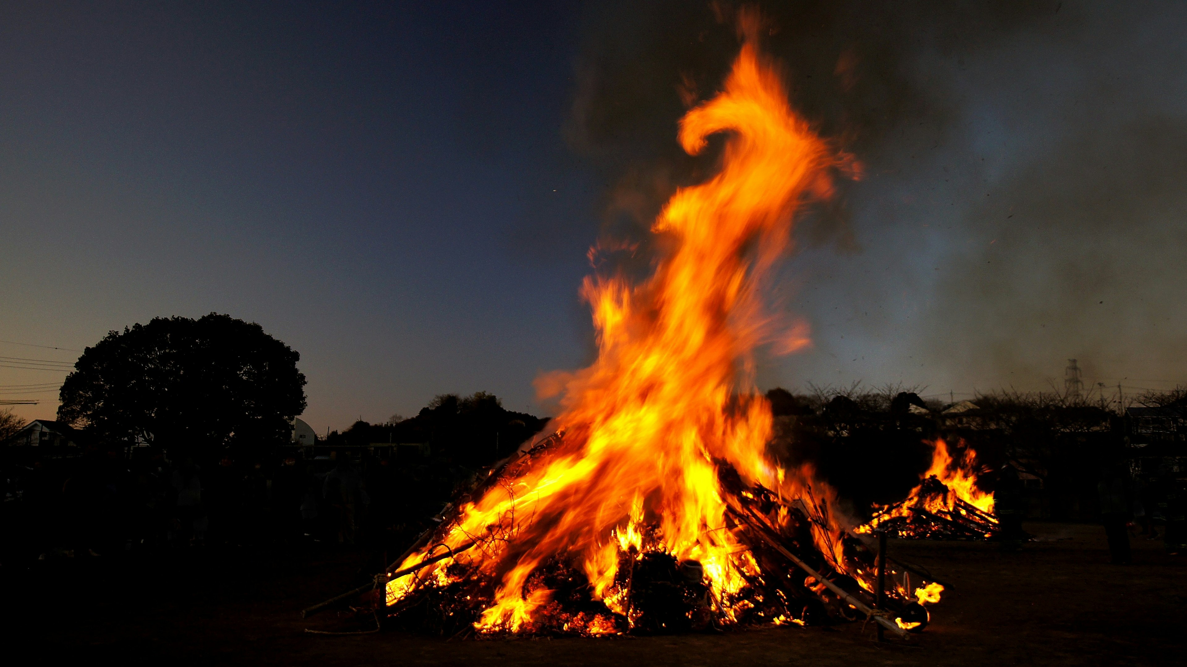 Large bonfire burning against a night sky with smoke