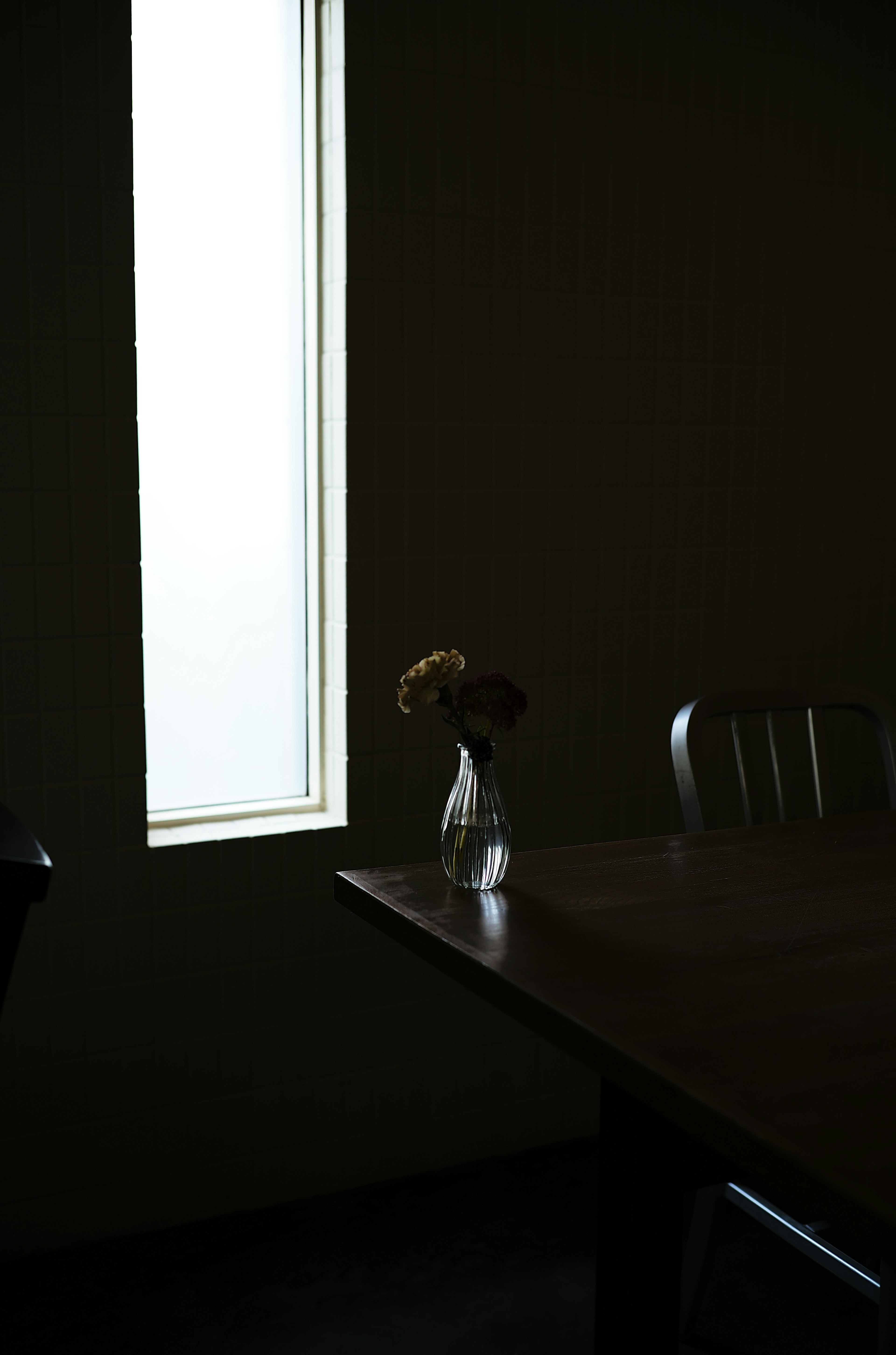 A dimly lit room with a vase on the table and light coming through the window