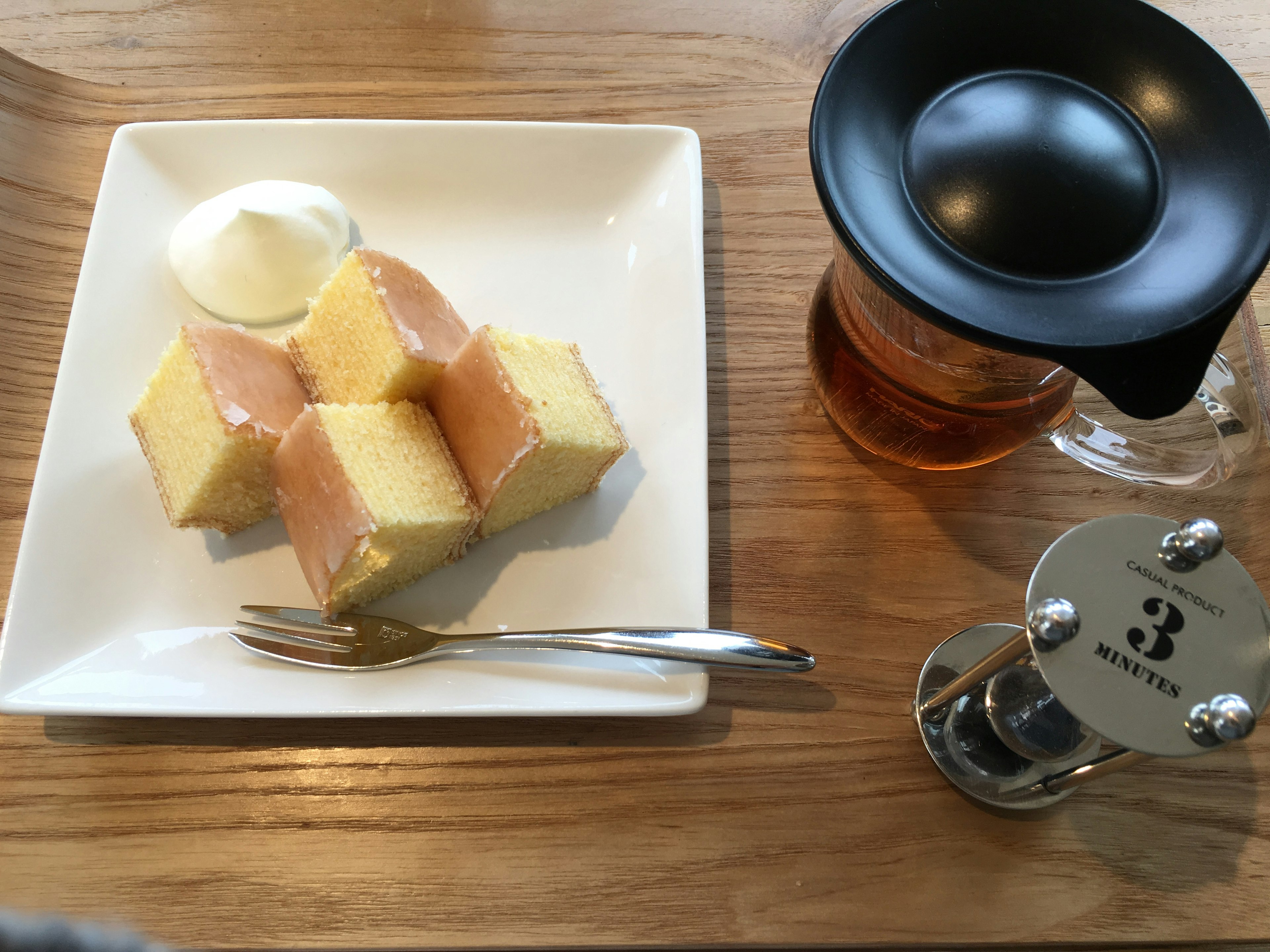 Square cake with cream served on a plate alongside a teapot and tea