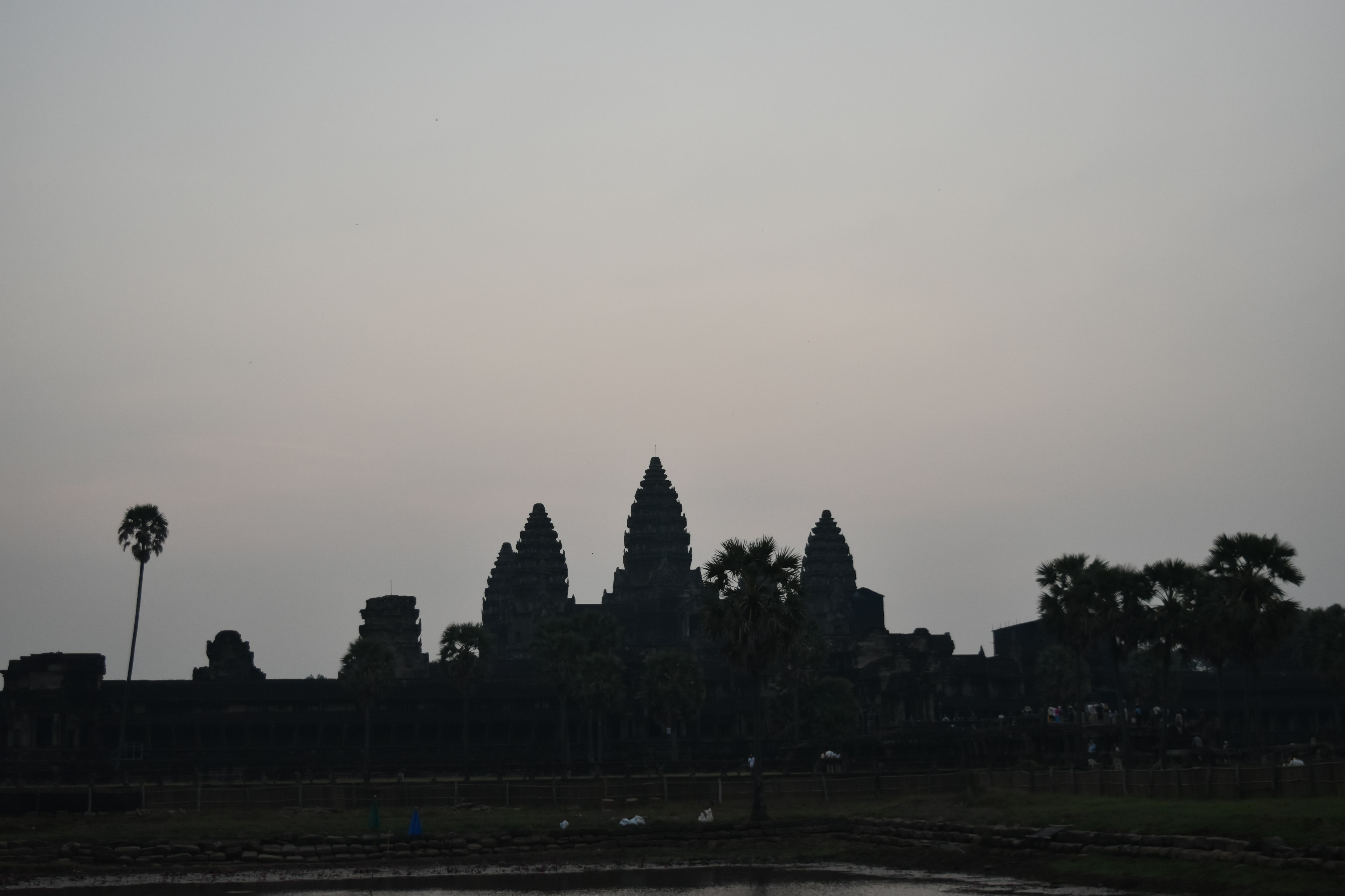 Silhouette of Angkor Wat at dusk with palm trees