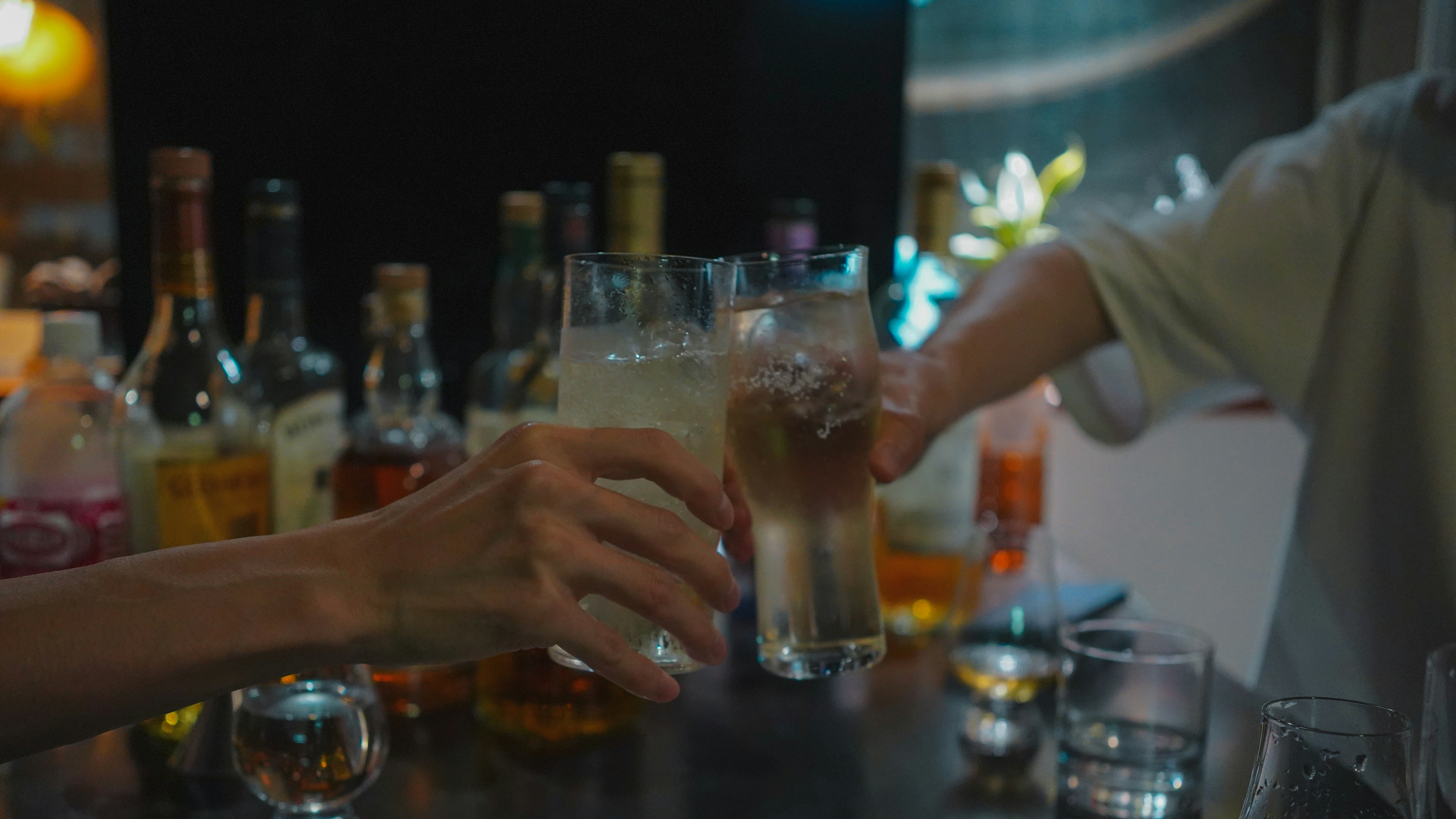 Un moment de toast avec des boissons à la main entouré de diverses bouteilles de liqueur