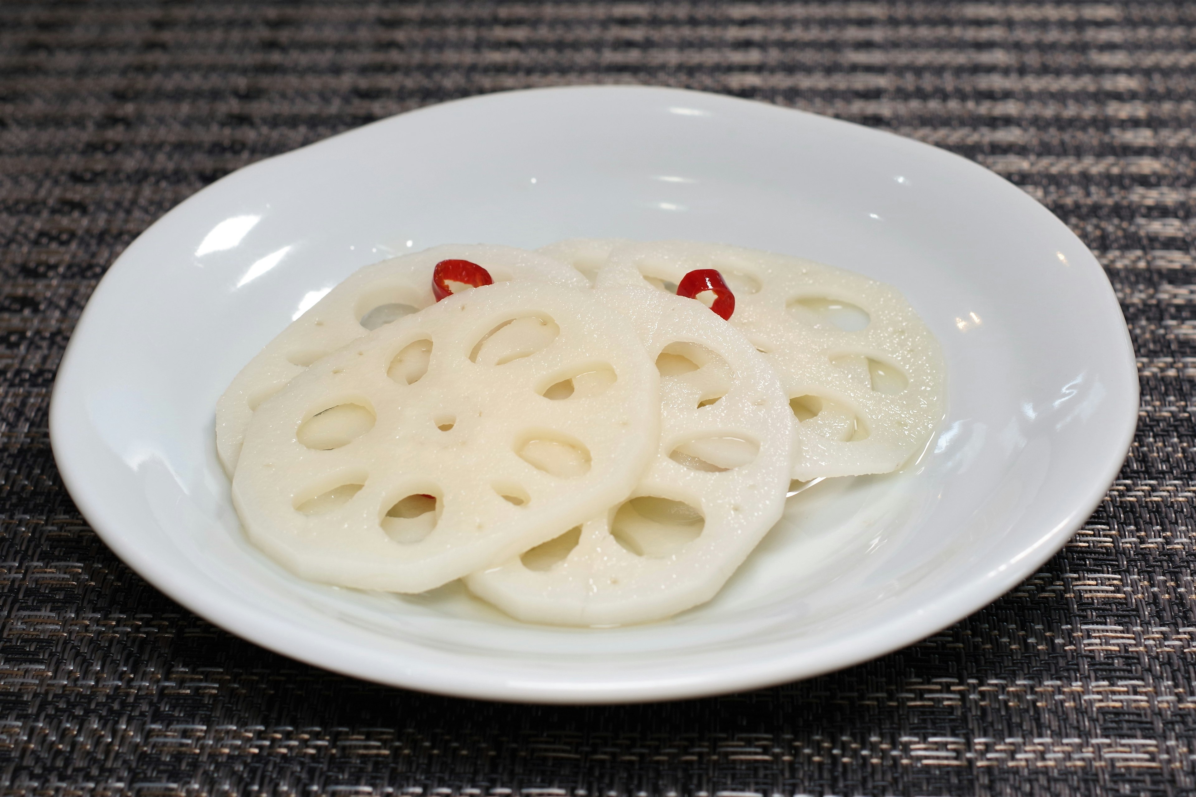 Rodajas de raíz de loto servidas en un plato blanco con guarnición de chile rojo