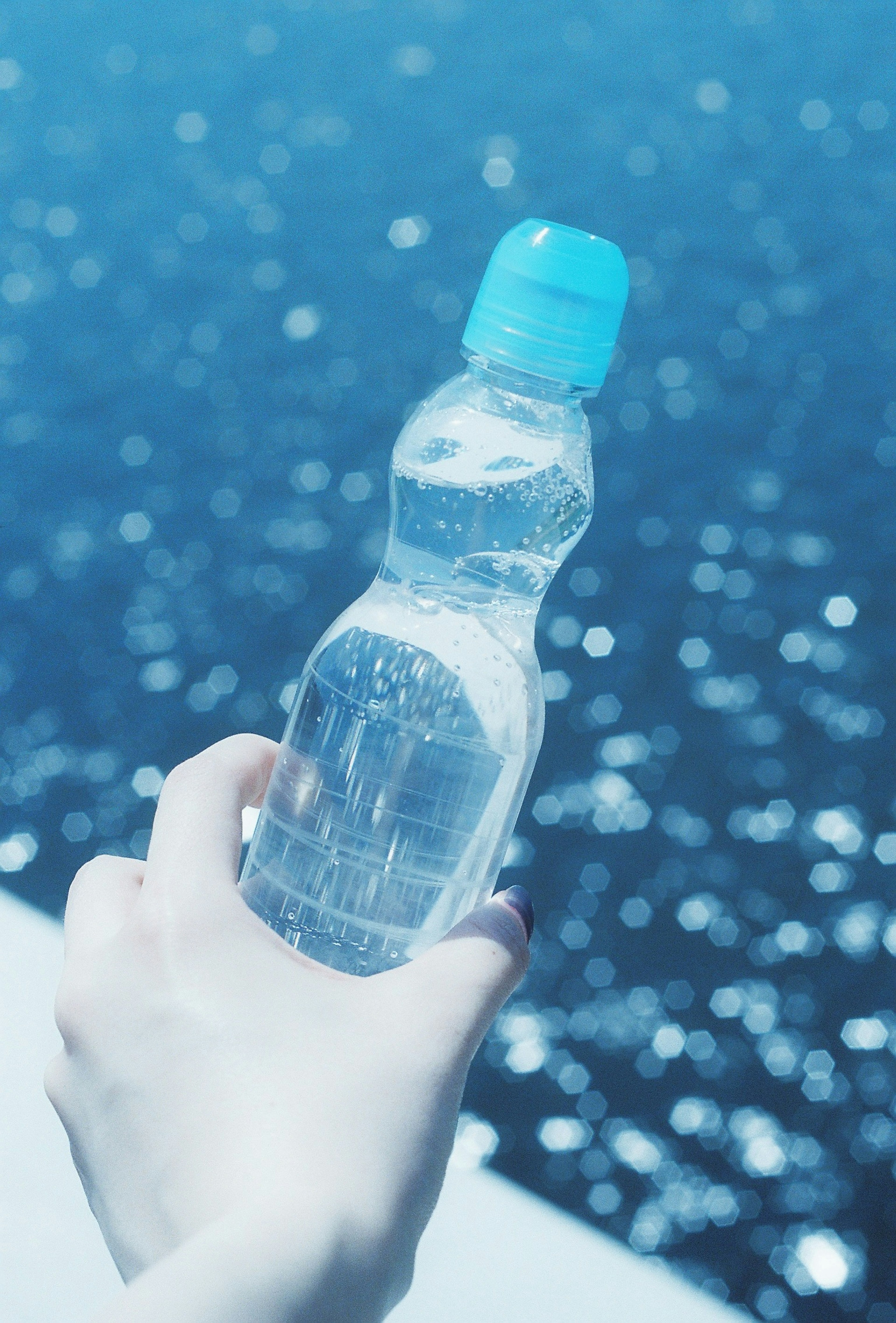 Main tenant une bouteille d'eau devant un fond océan bleu