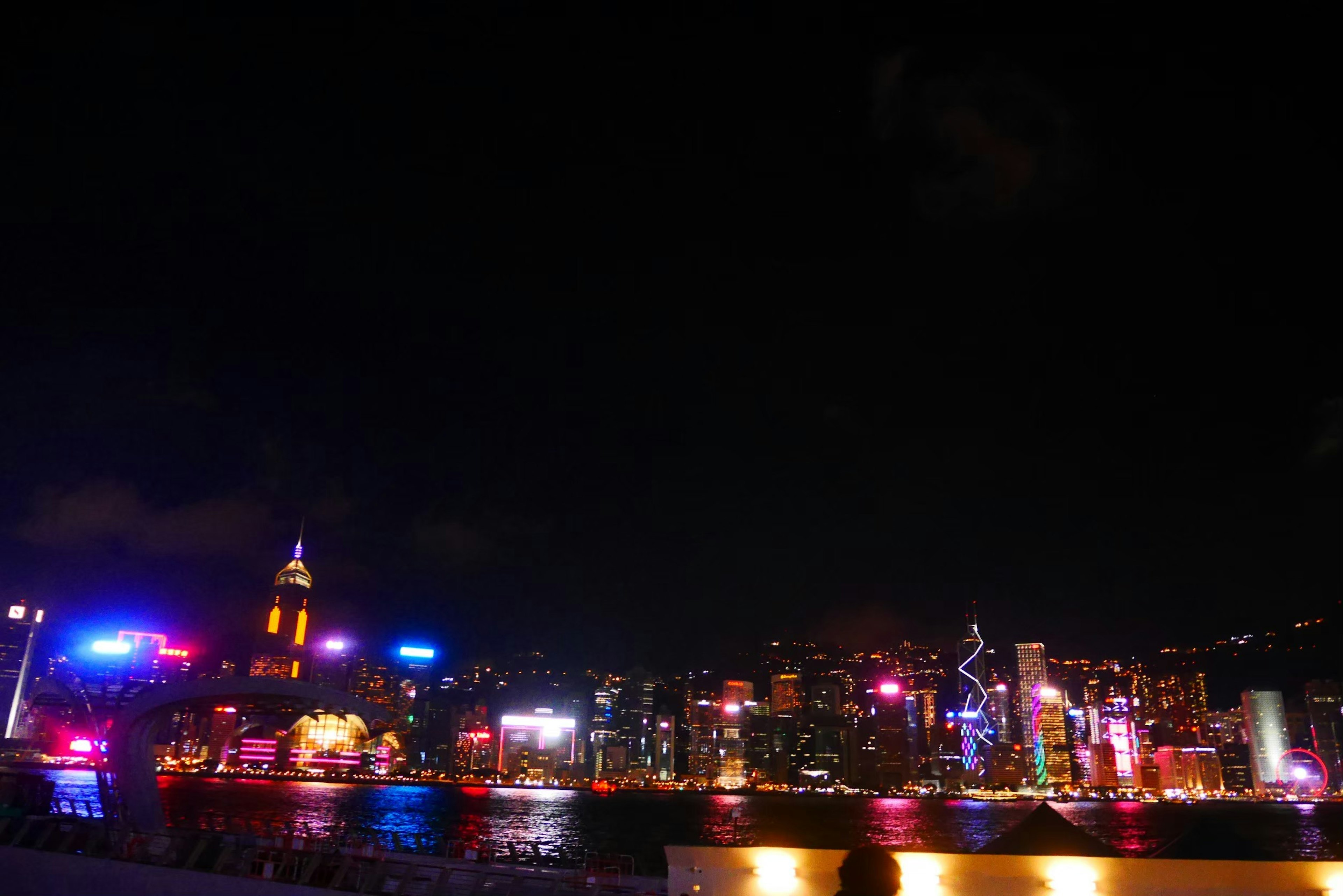 Die Skyline von Hongkong bei Nacht mit bunten Lichtern und Gebäudesilhouetten, die sich im Victoria Harbour spiegeln