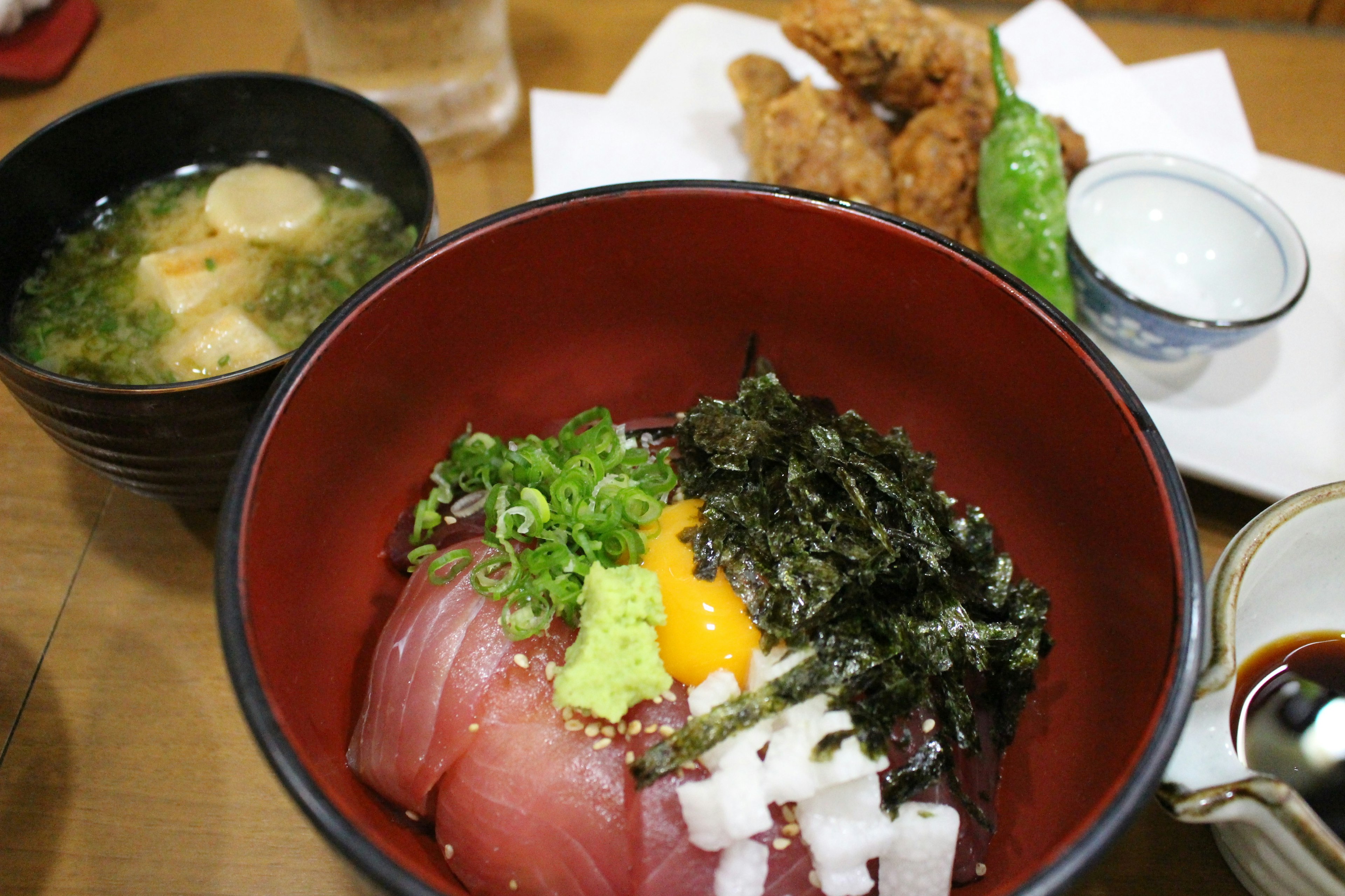 A bowl of fresh sashimi topped with seaweed, wasabi, and egg yolk served with miso soup and fried chicken