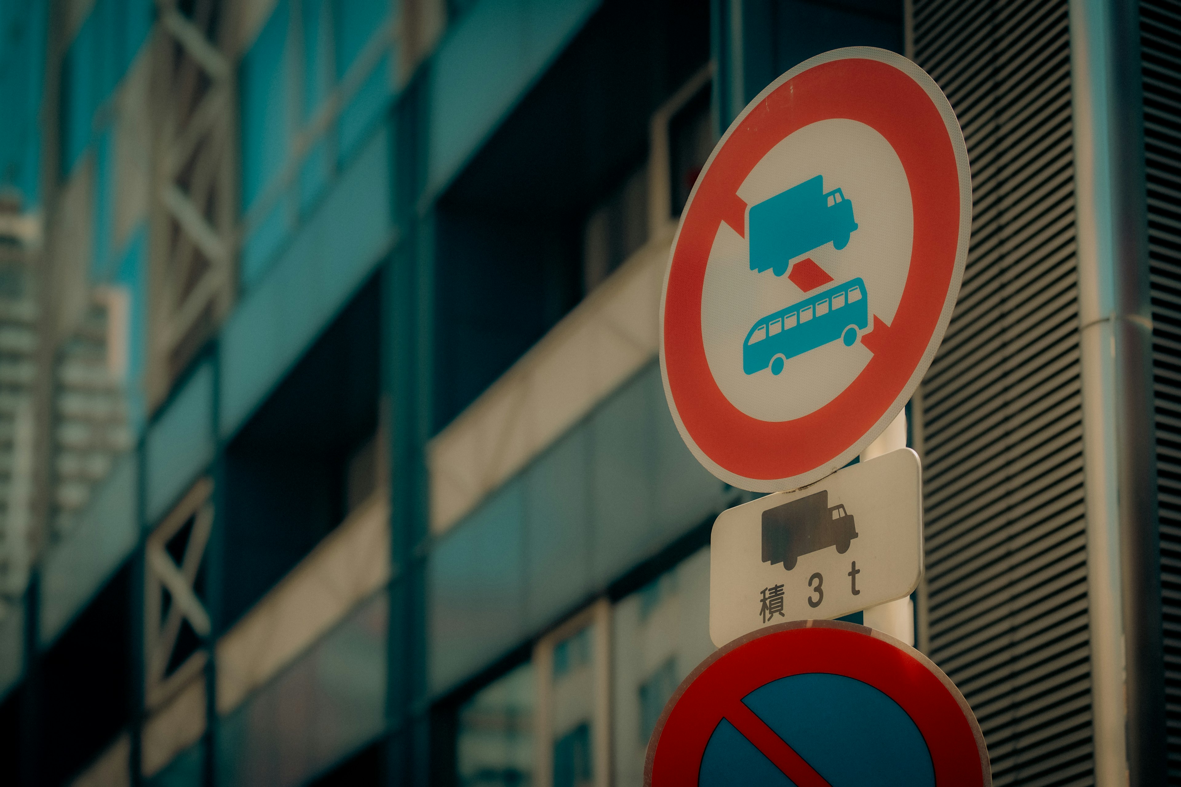 Traffic signs indicating no parking for trucks and buses next to a modern blue building