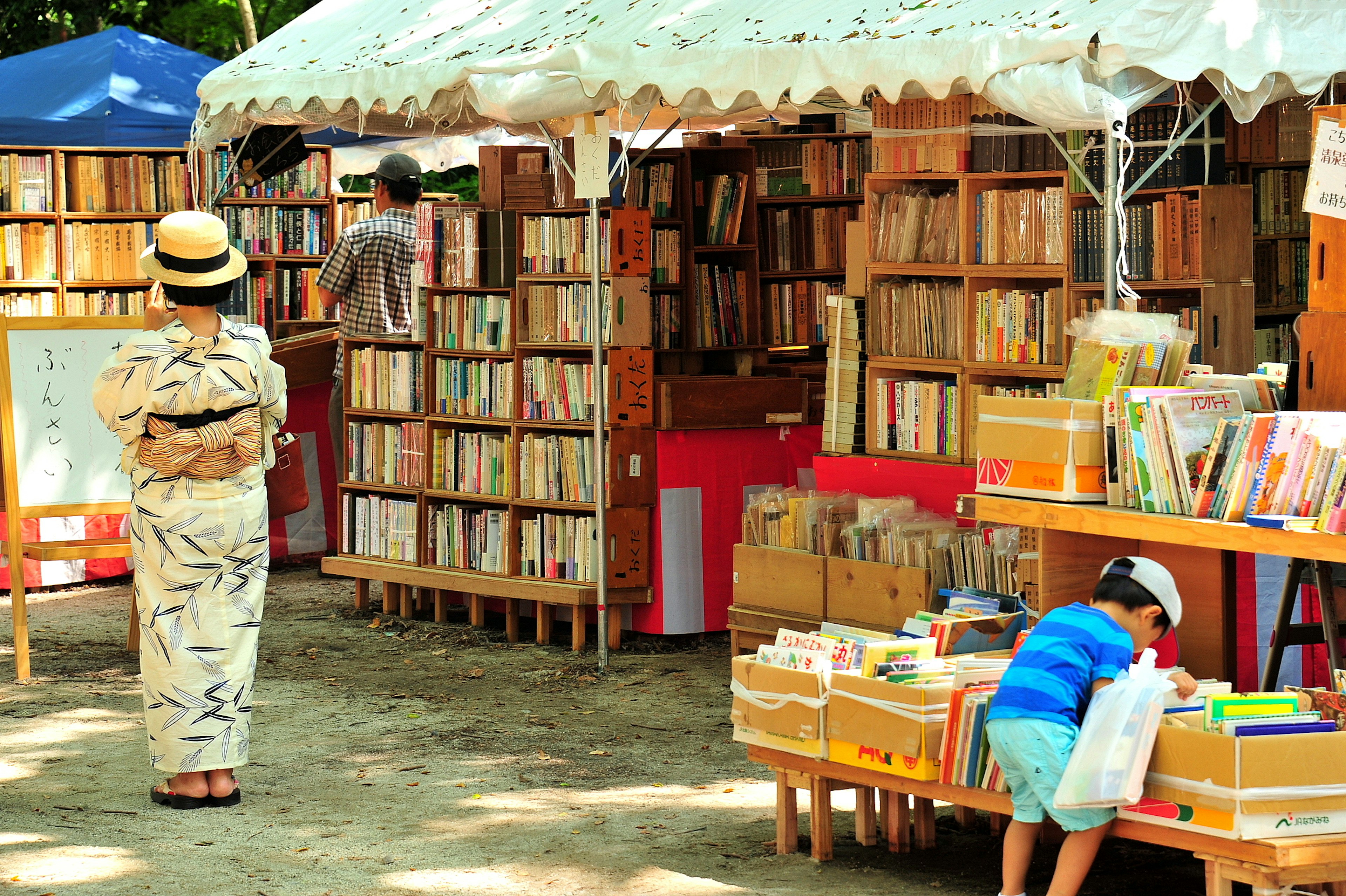 Una mujer en kimono y un niño buscando libros en una feria de libros al aire libre