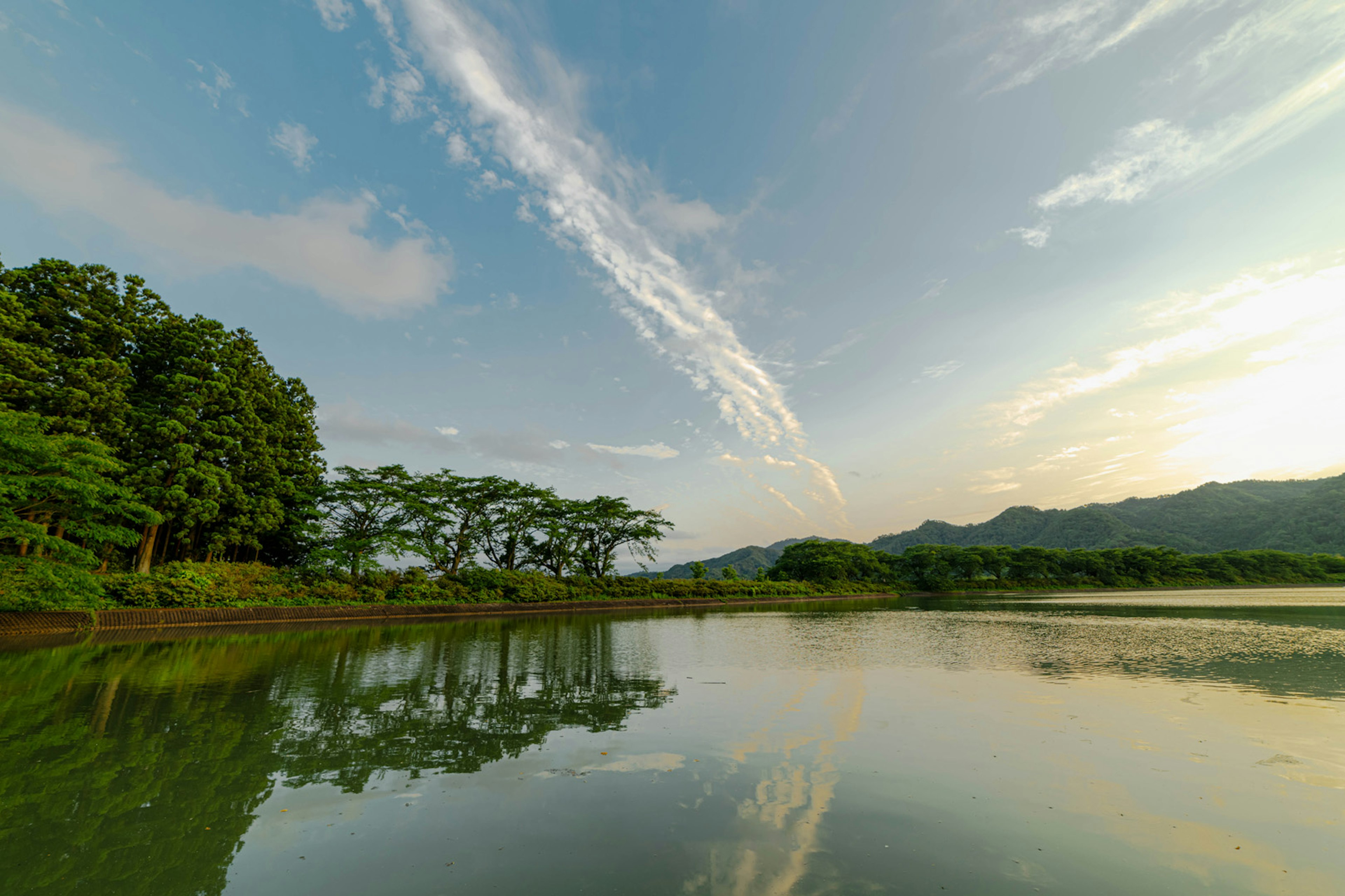 ทิวทัศน์ที่เงียบสงบมีทะเลสาบที่สงบและการสะท้อน ท้องฟ้าสีฟ้าพร้อมรูปแบบเมฆที่โดดเด่น