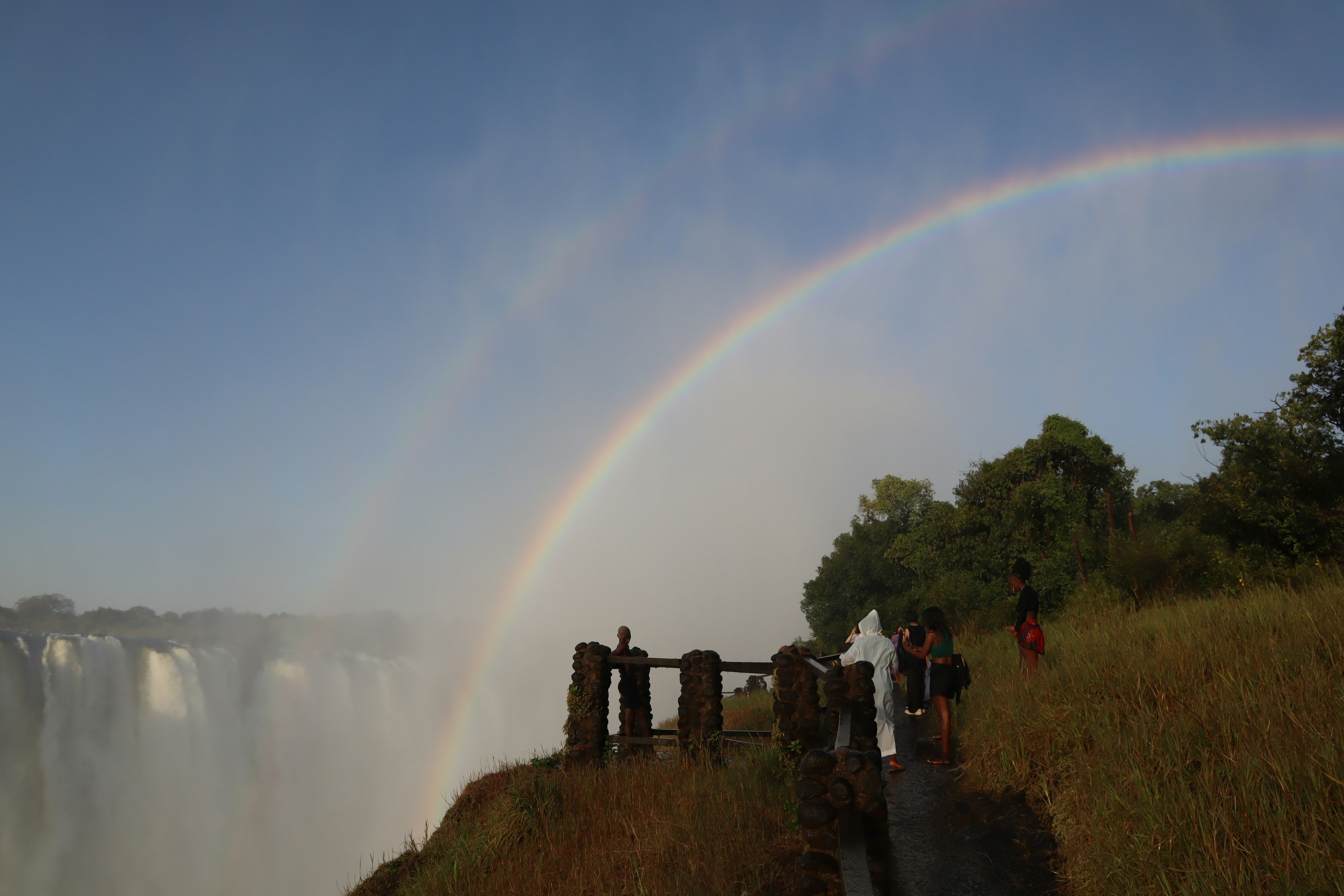 Arcoíris sobre una cascada con turistas en silueta