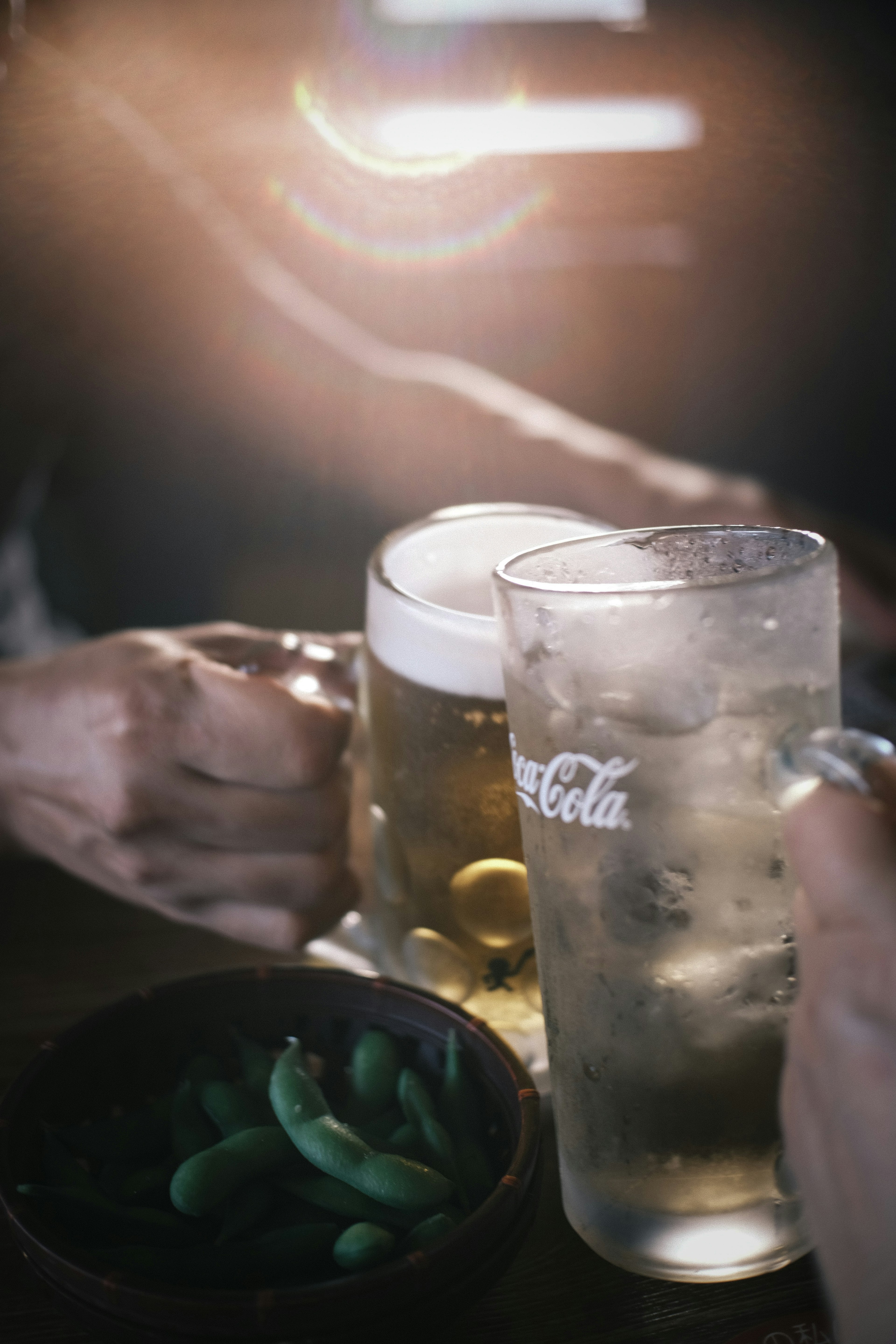 Gambar menunjukkan tangan memegang gelas bir dan Coca-Cola