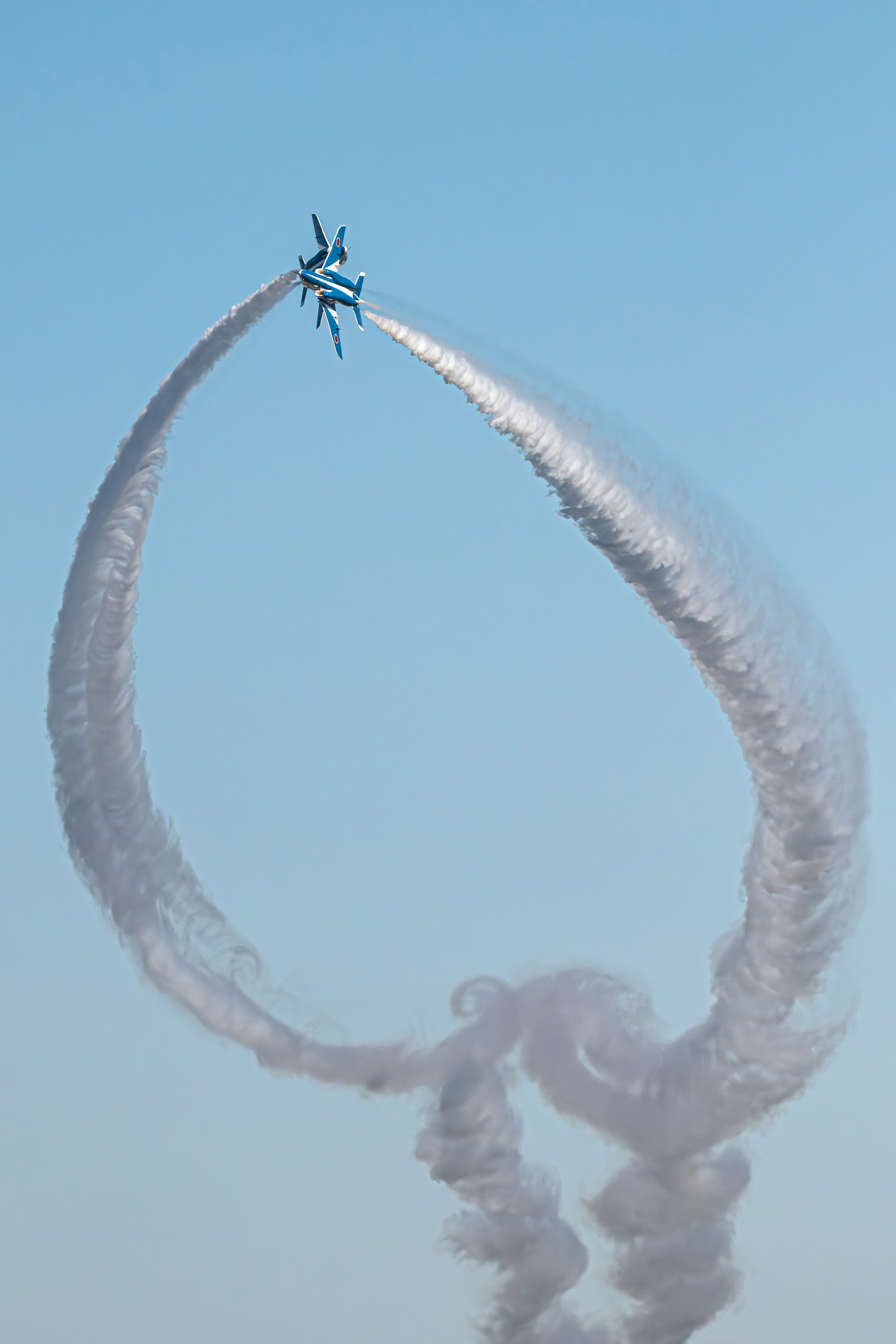 Aereo che crea una scia di fumo circolare nel cielo blu