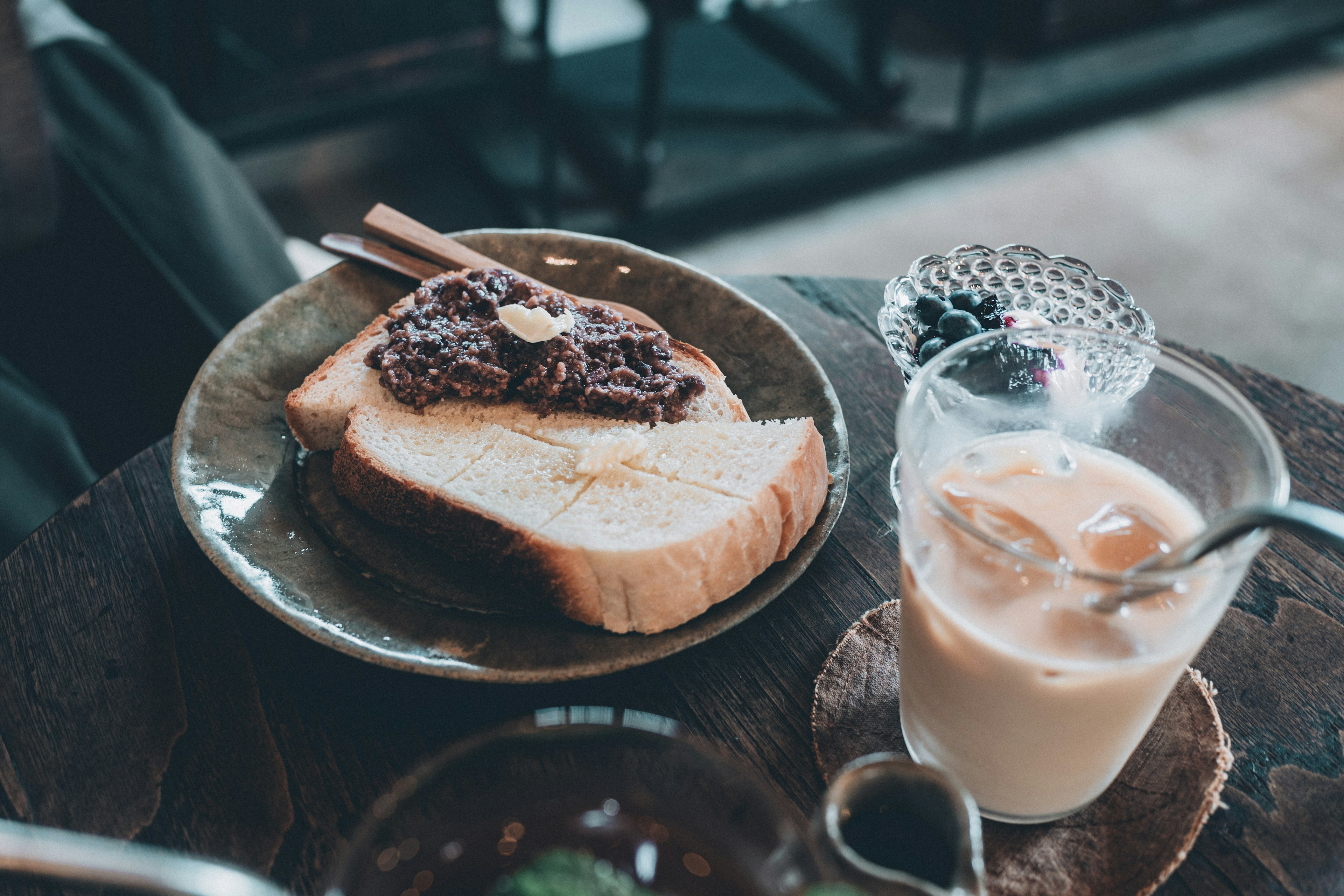 Piring dengan roti panggang yang ditutup pasta kacang merah dan segelas kopi es