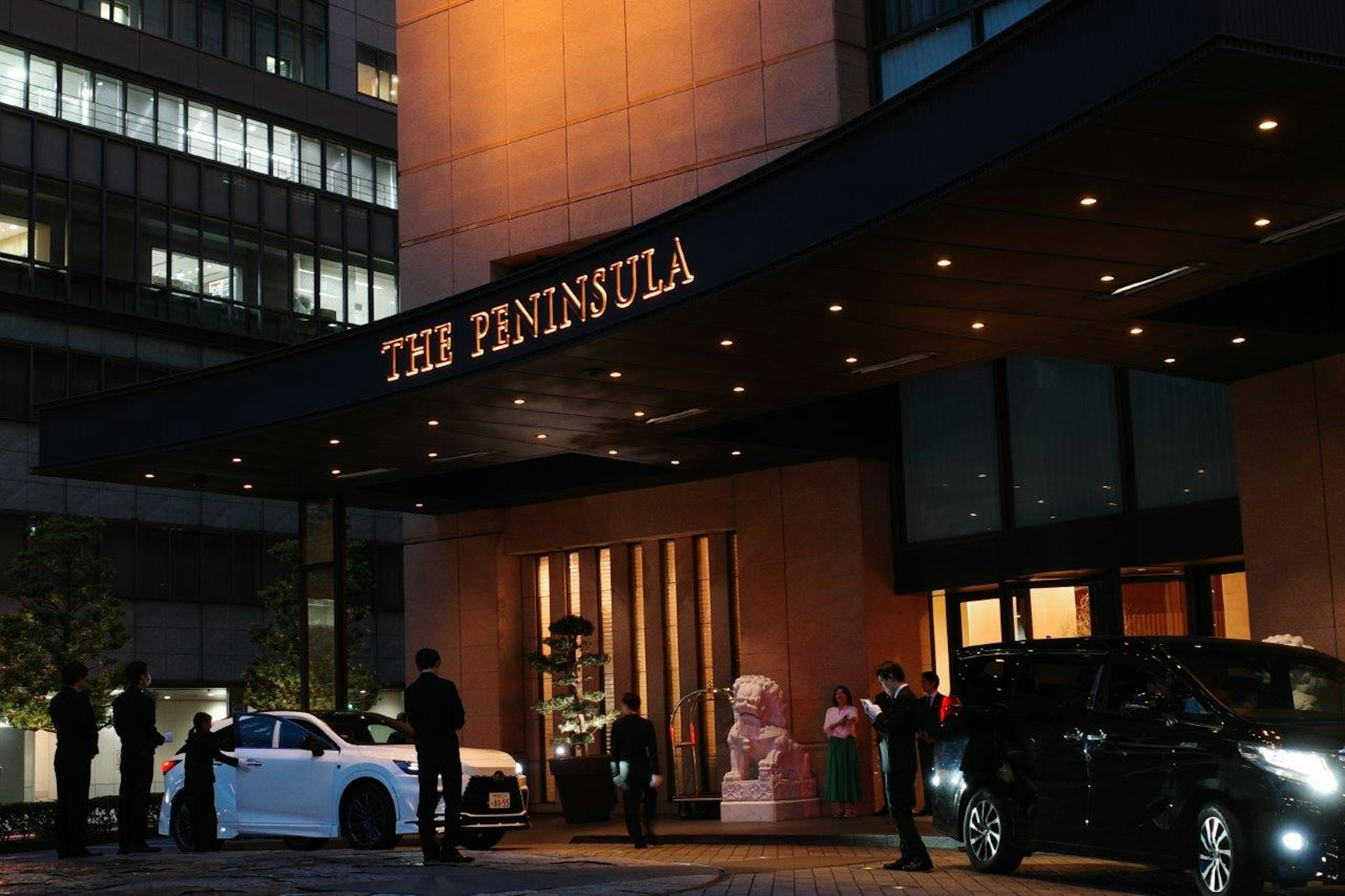 Eingang des Peninsula Hotels bei Nacht mit wartenden Autos und Personal