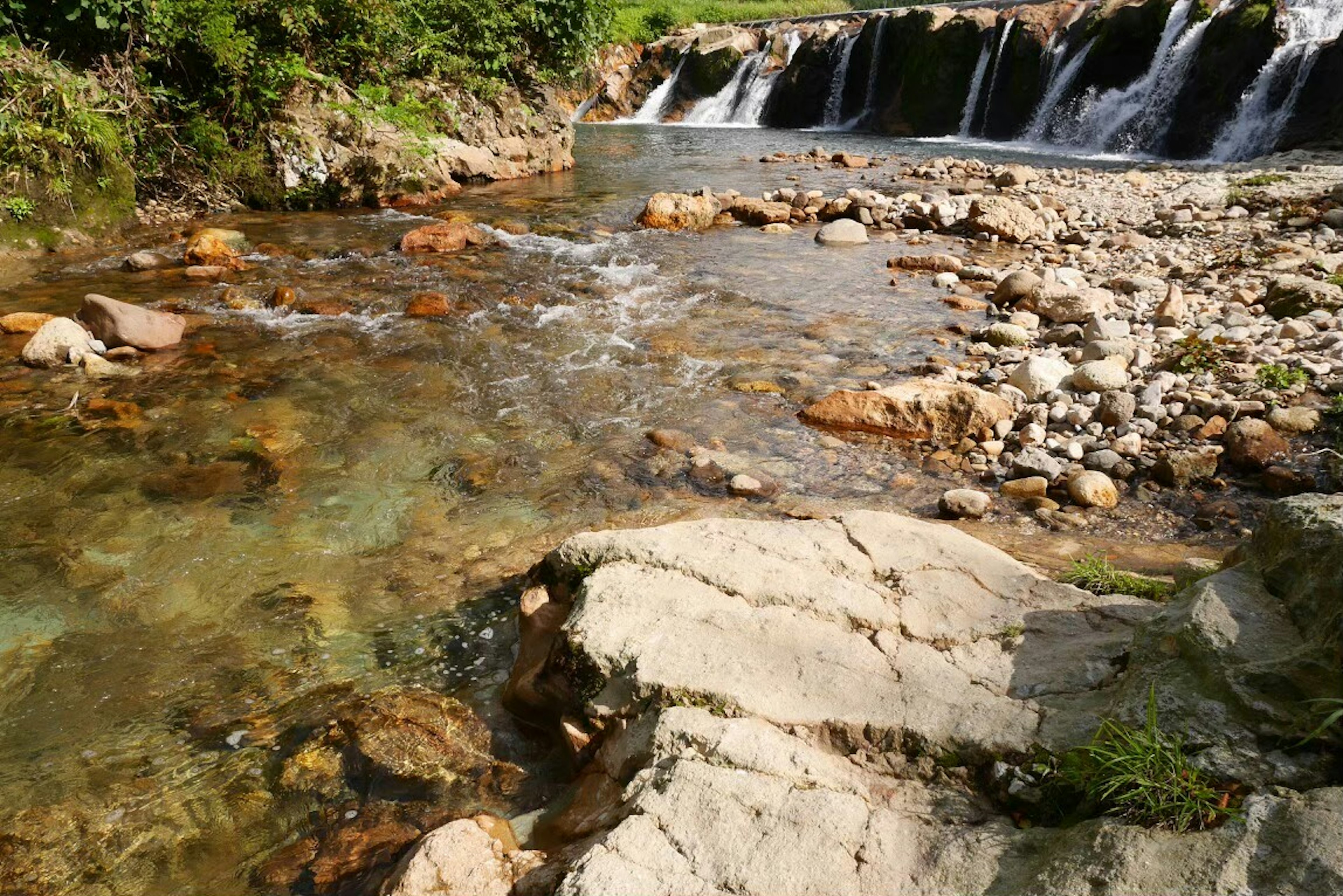 Clear water flowing over rocks and a small waterfall in a natural setting