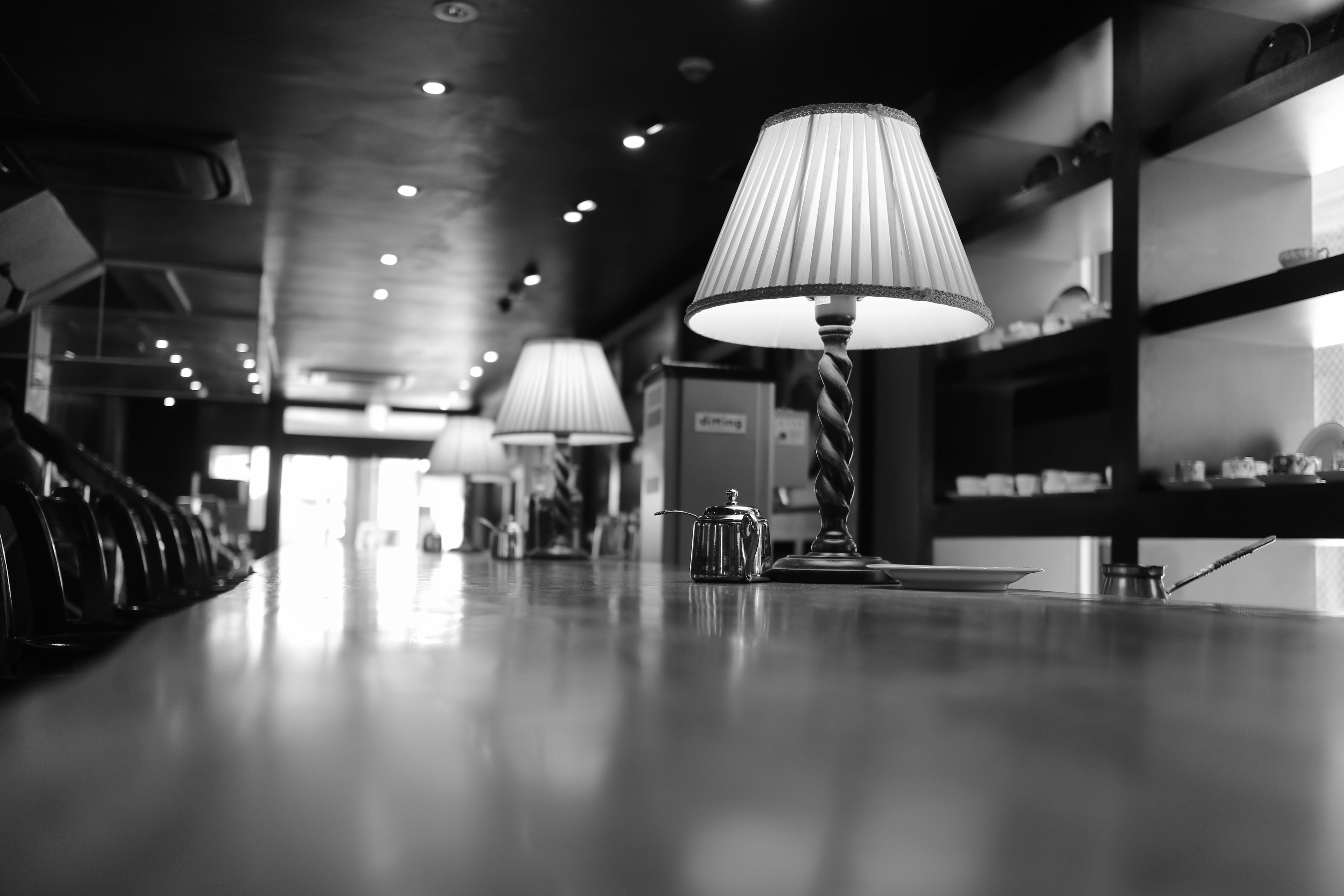 Black and white photo of a stylish cafe interior featuring lamps on a table and shelves in the background