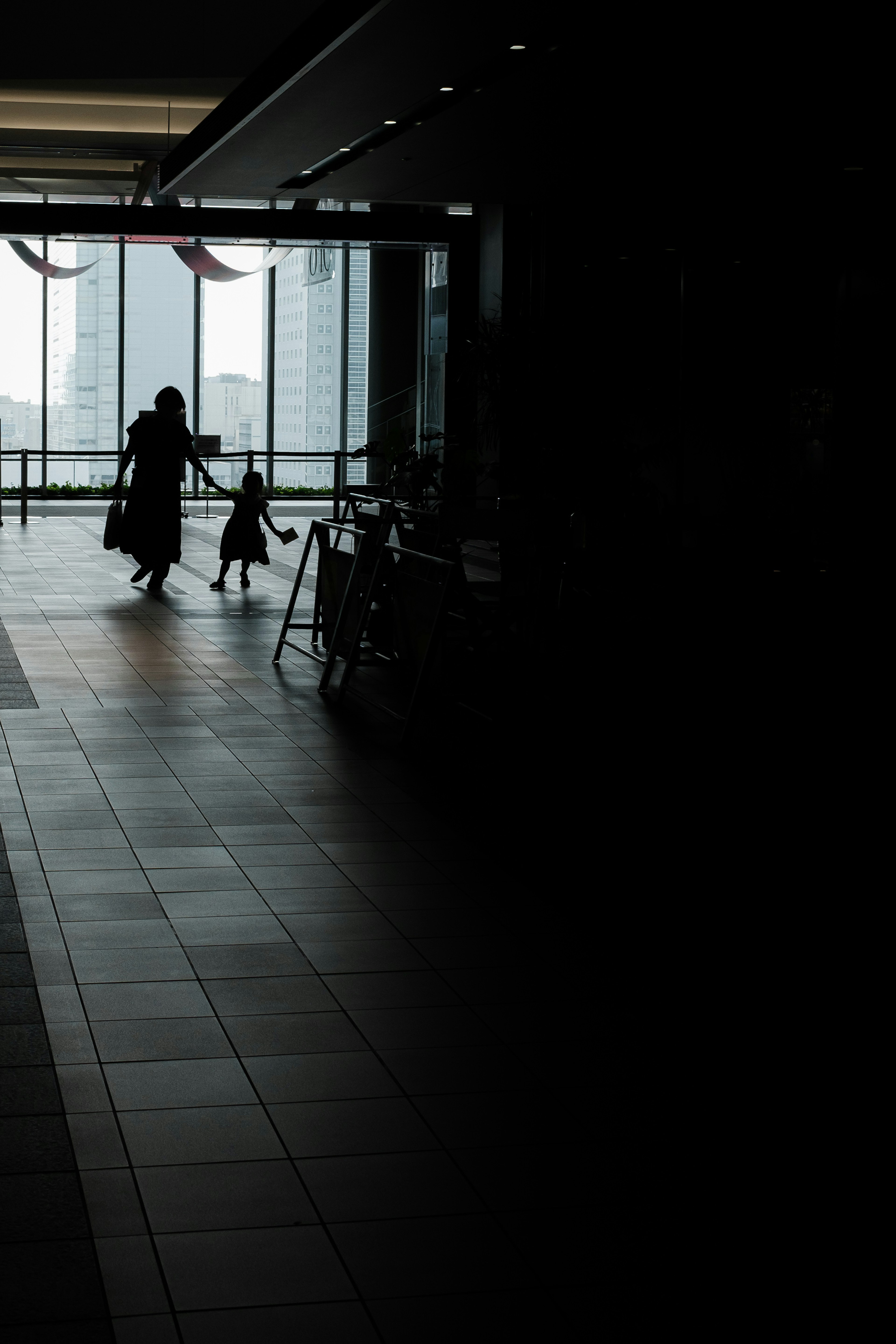 Silhouette einer Mutter und eines Kindes, die in einem dunklen Innenraum mit natürlichem Licht, das durch Fenster strömt, gehen