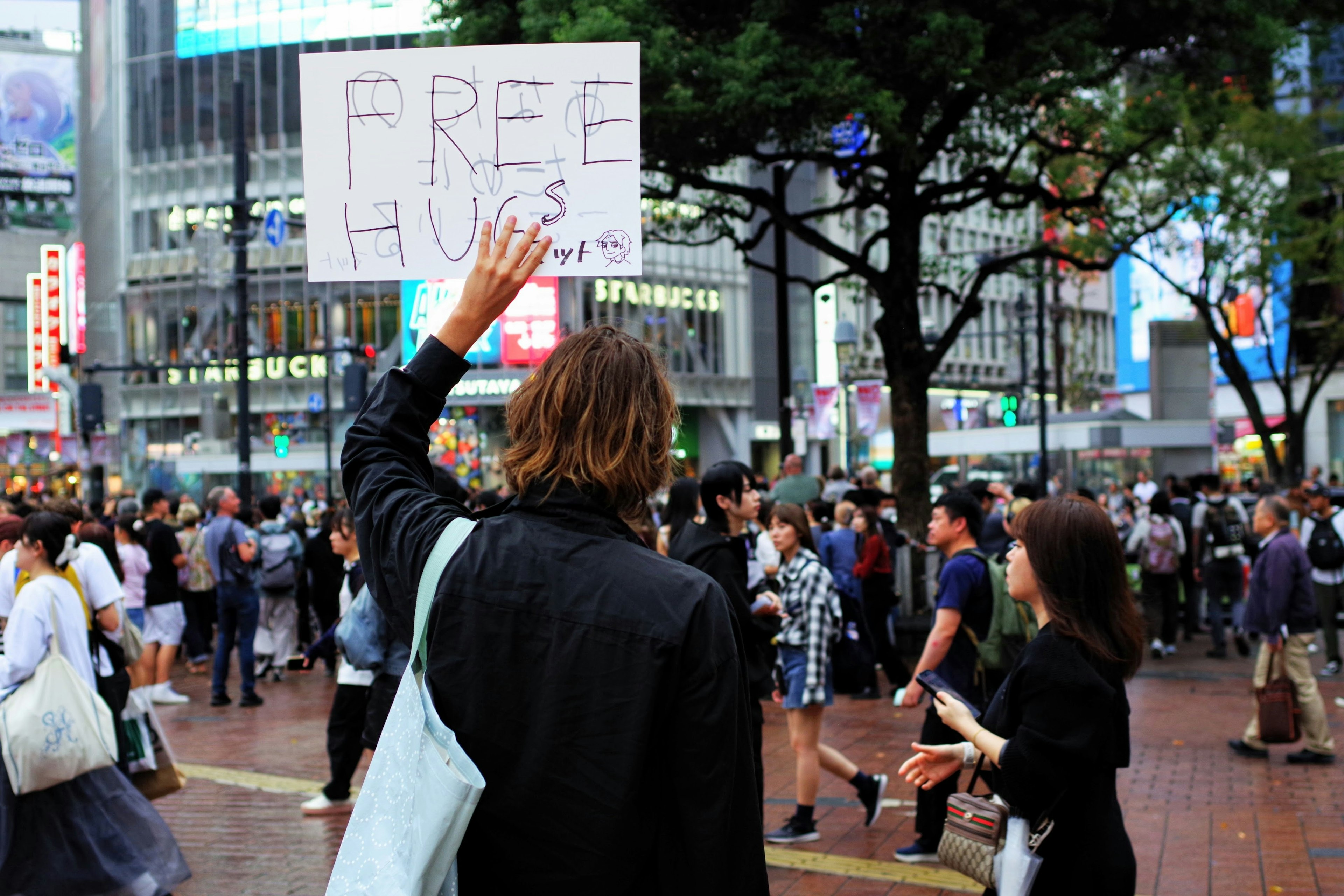 Persona che tiene un cartello con scritto FREE HUGS in una zona urbana affollata