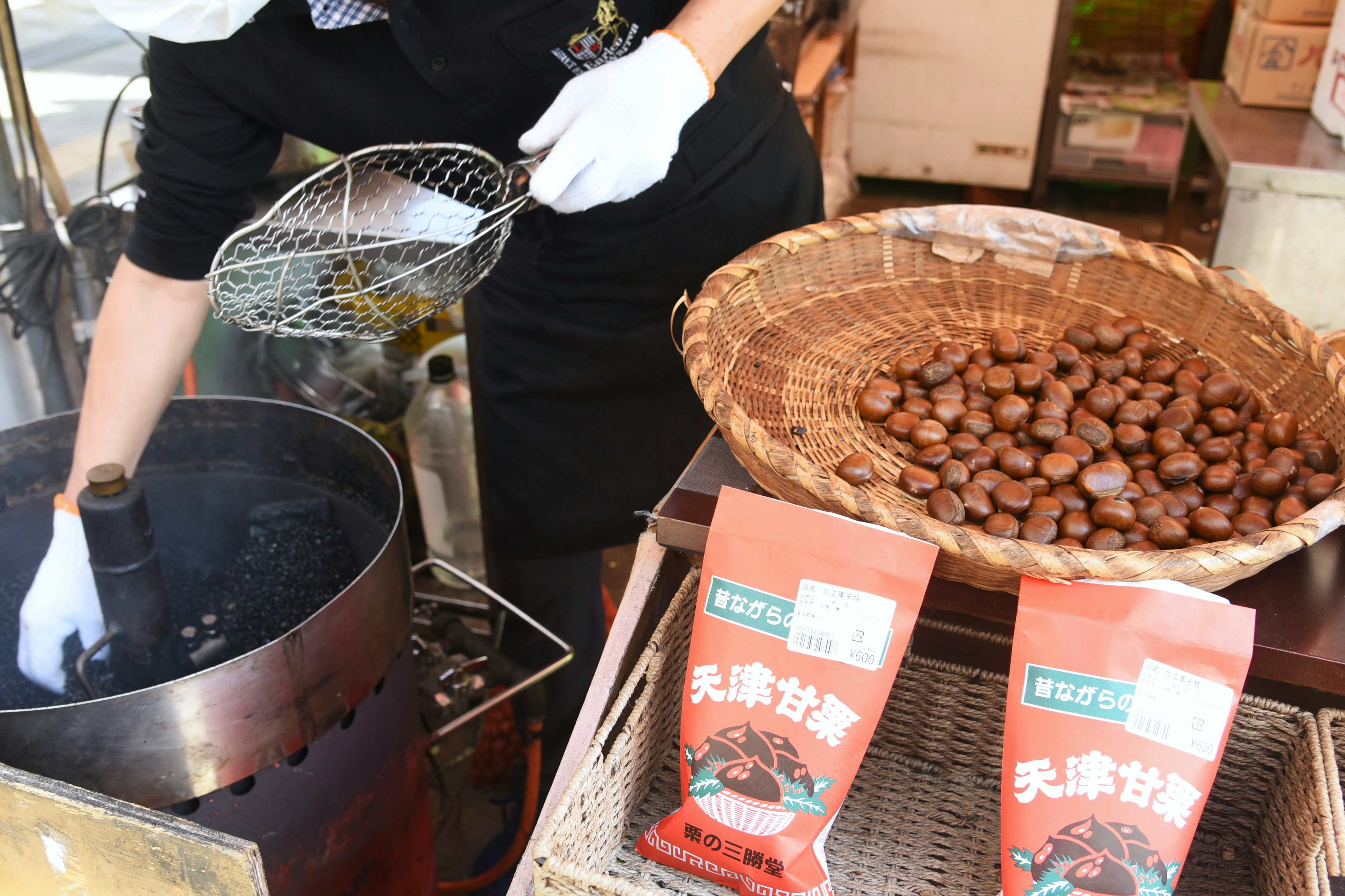 Seseorang sedang memasak kastanye dalam panci dengan kemasan kastanye dipajang di dekatnya