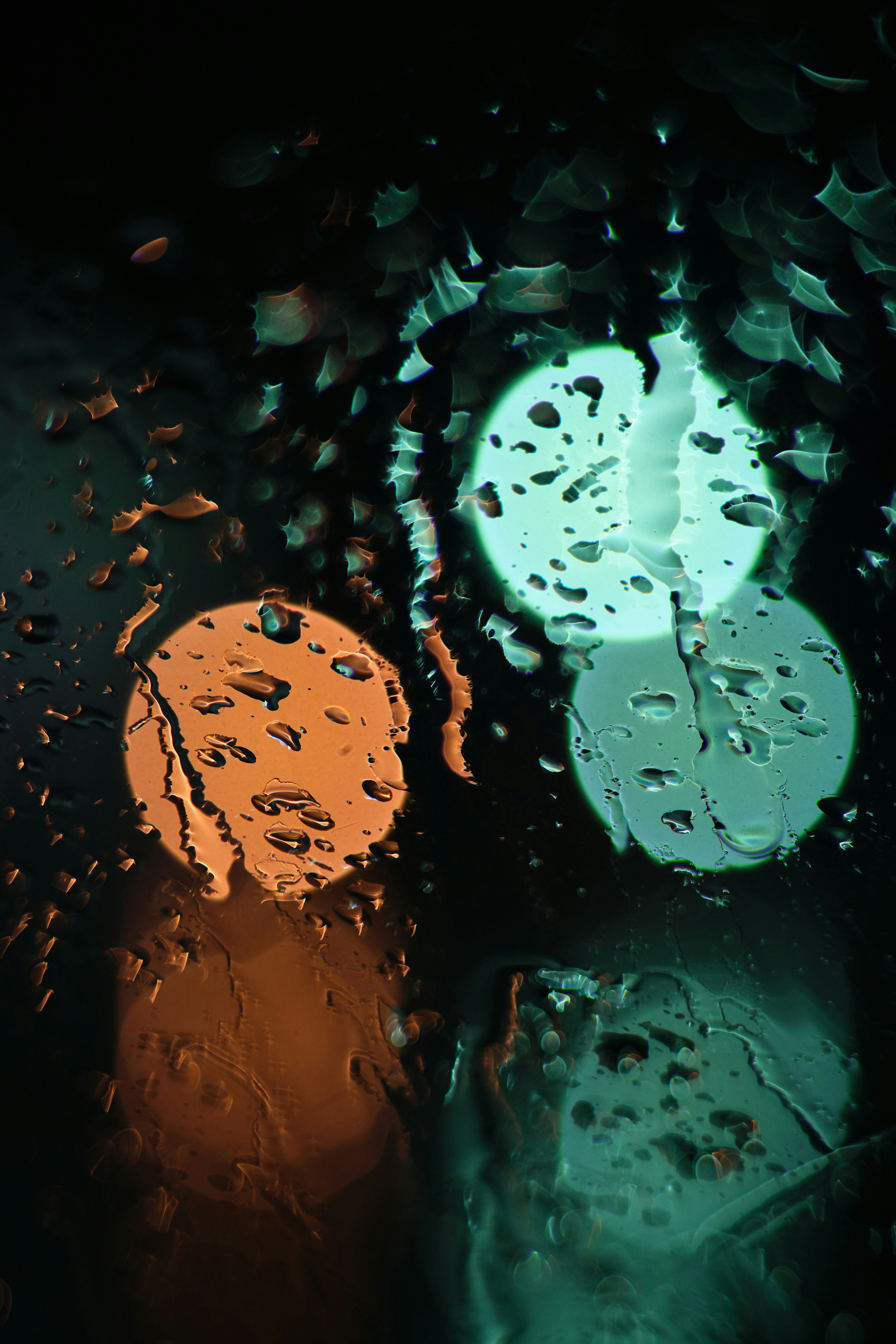 Blurry orange and green lights seen through raindrop-covered glass