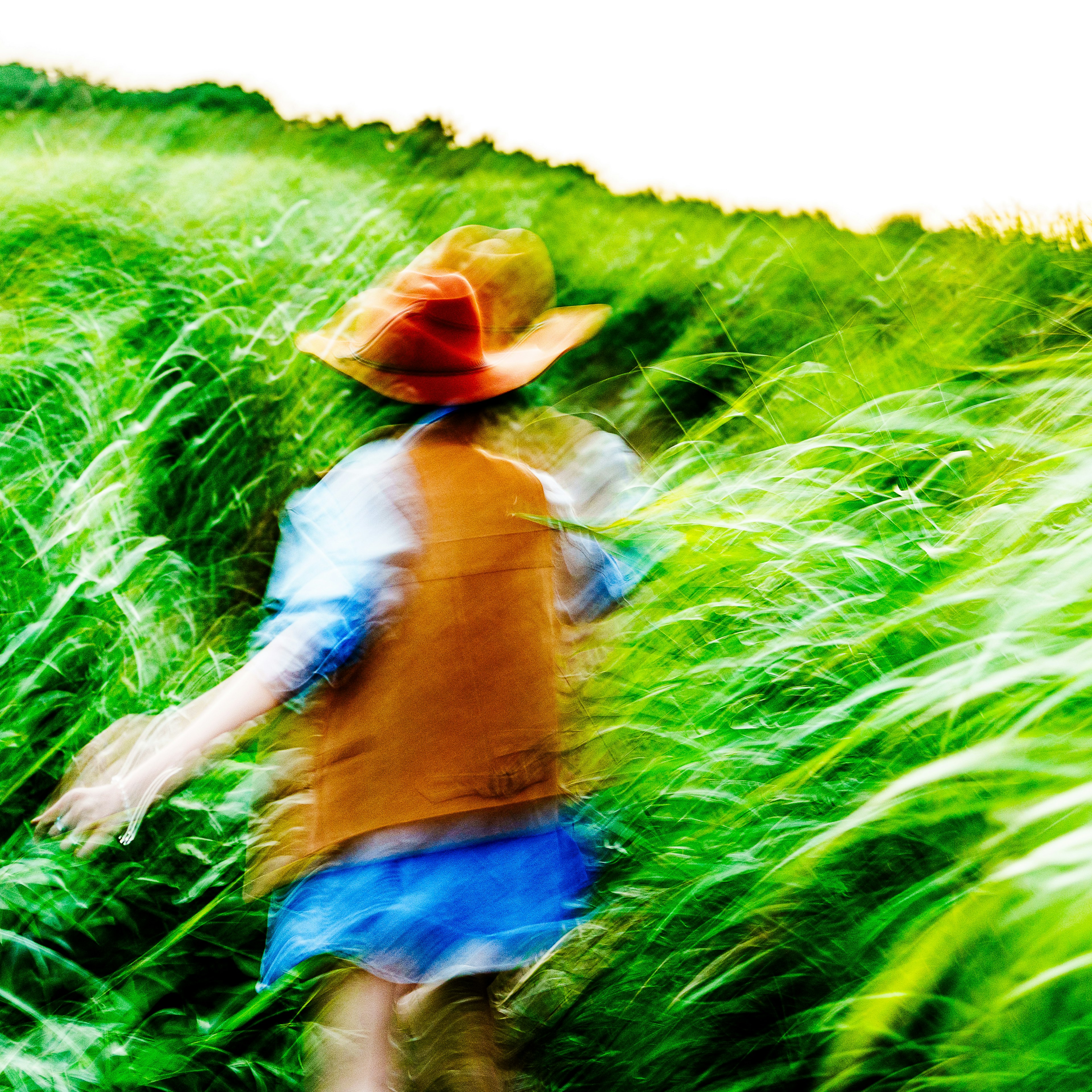 Kind, das durch ein grünes Feld rennt, trägt einen roten Hut und eine braune Weste