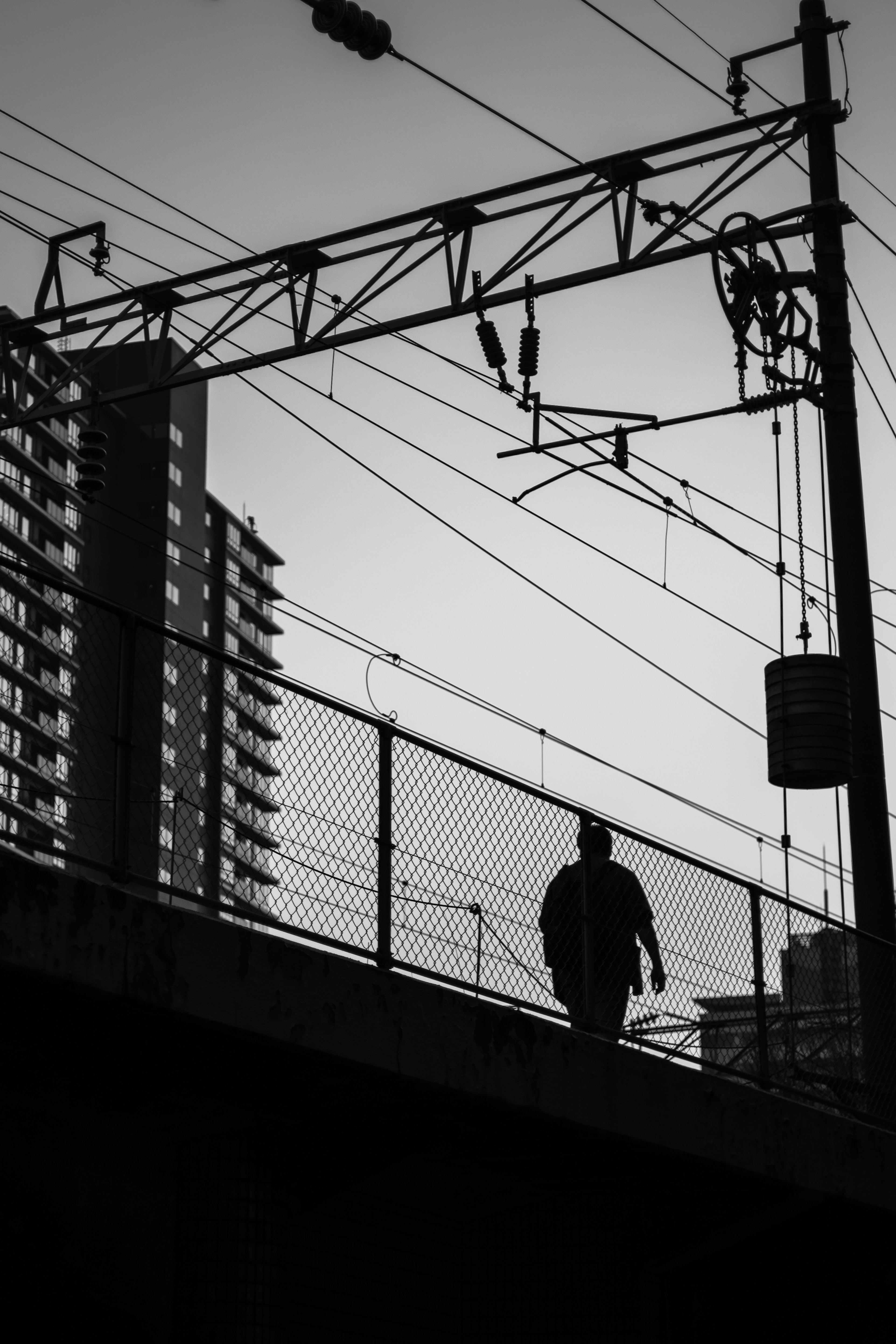 在鐵路橋上行走的男性輪廓，背景是城市建築和電線