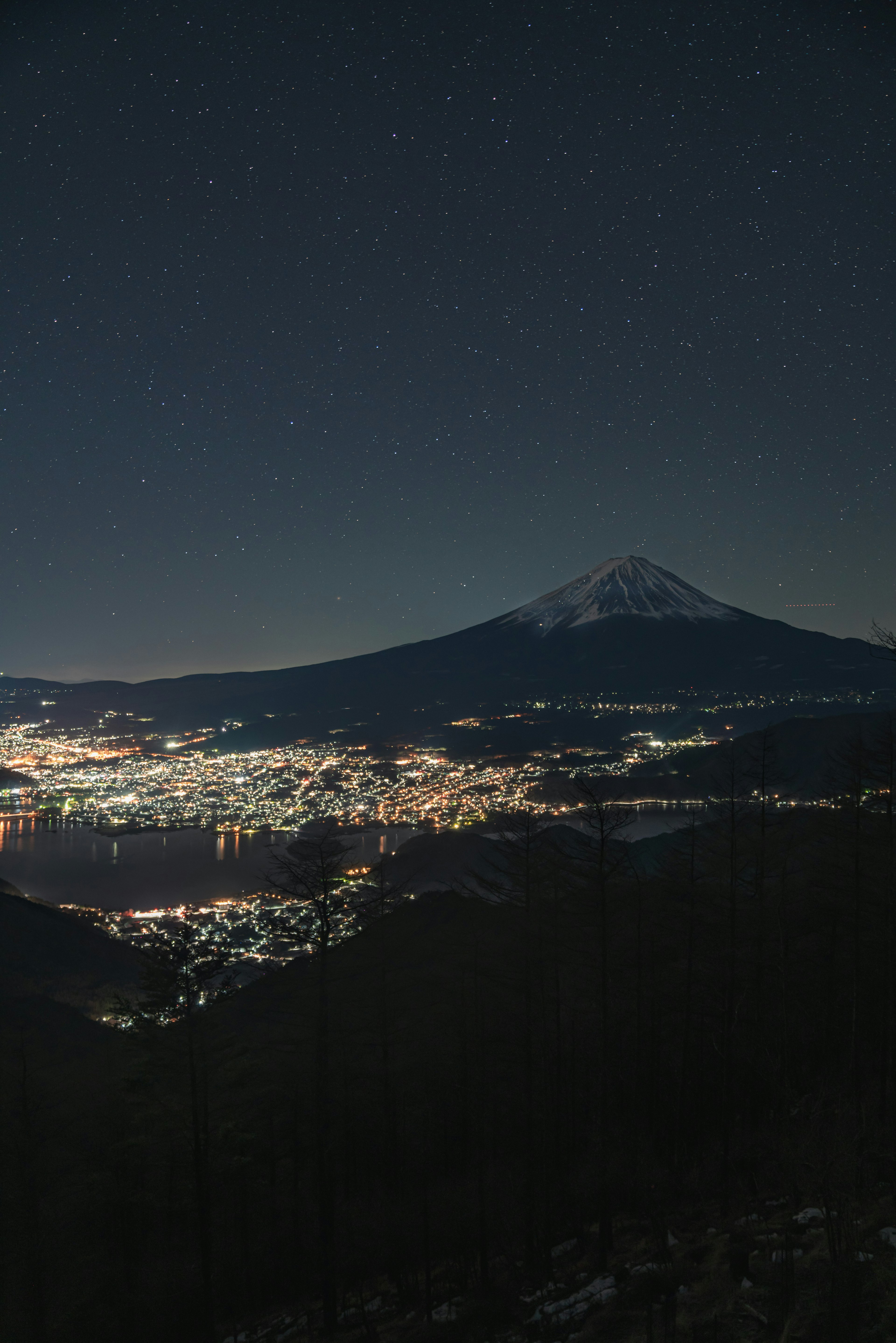 Vista nocturna del Monte Fuji con estrellas y luces de la ciudad