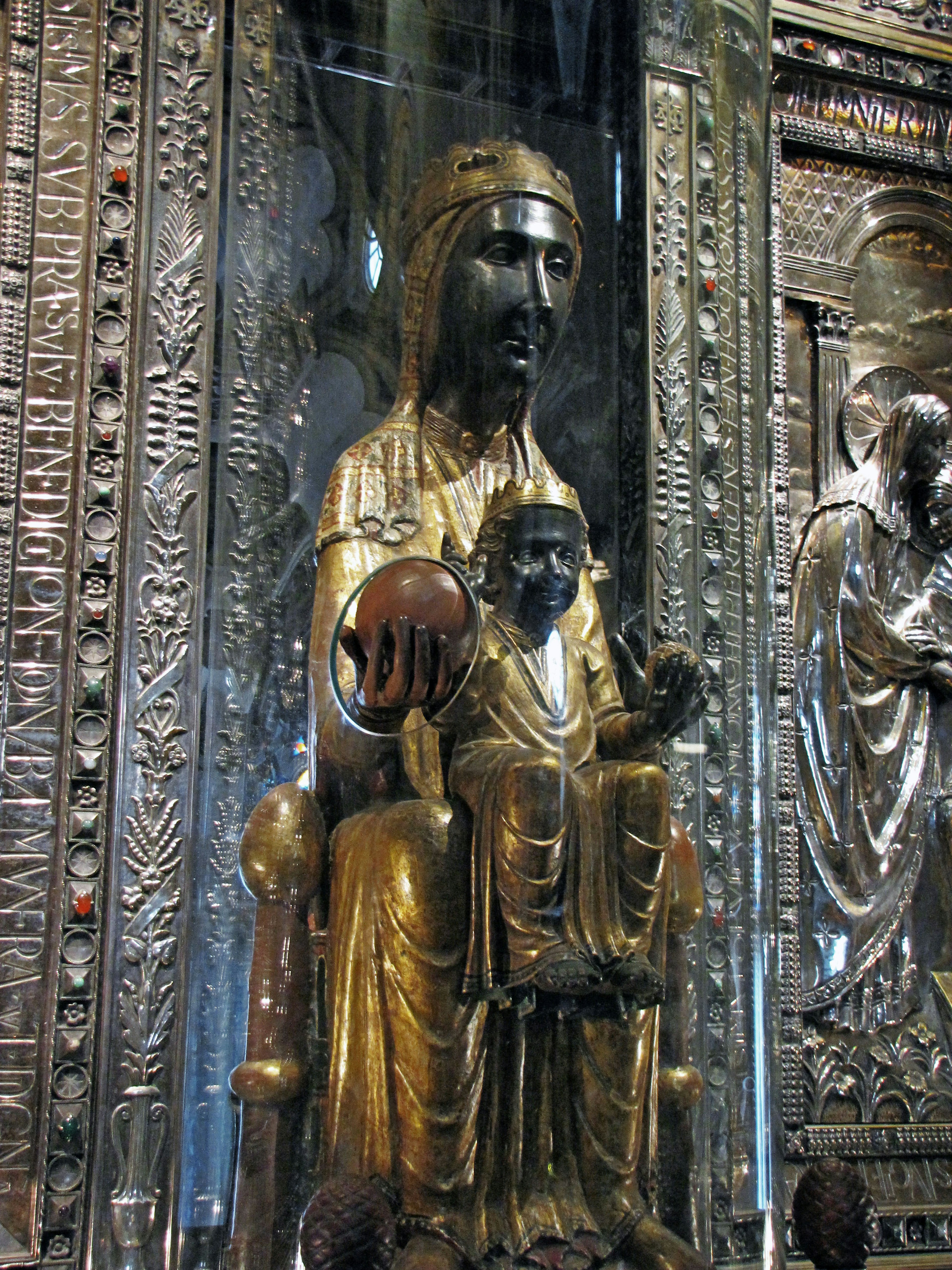 Estatua dorada de la Virgen María sosteniendo al niño Jesús en un entorno ricamente decorado