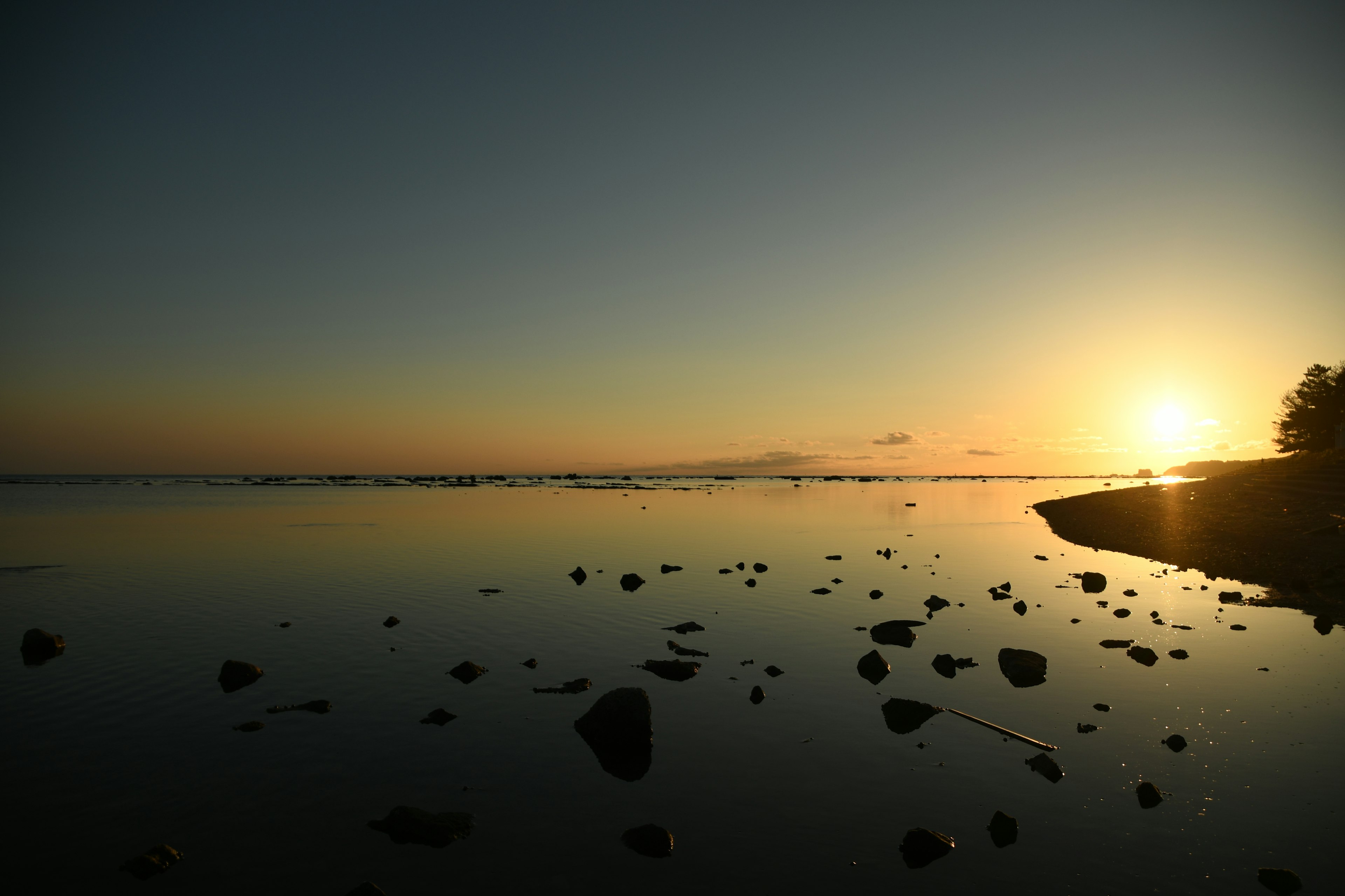 Ruhiger Sonnenuntergang über ruhigem Wasser mit Steinen