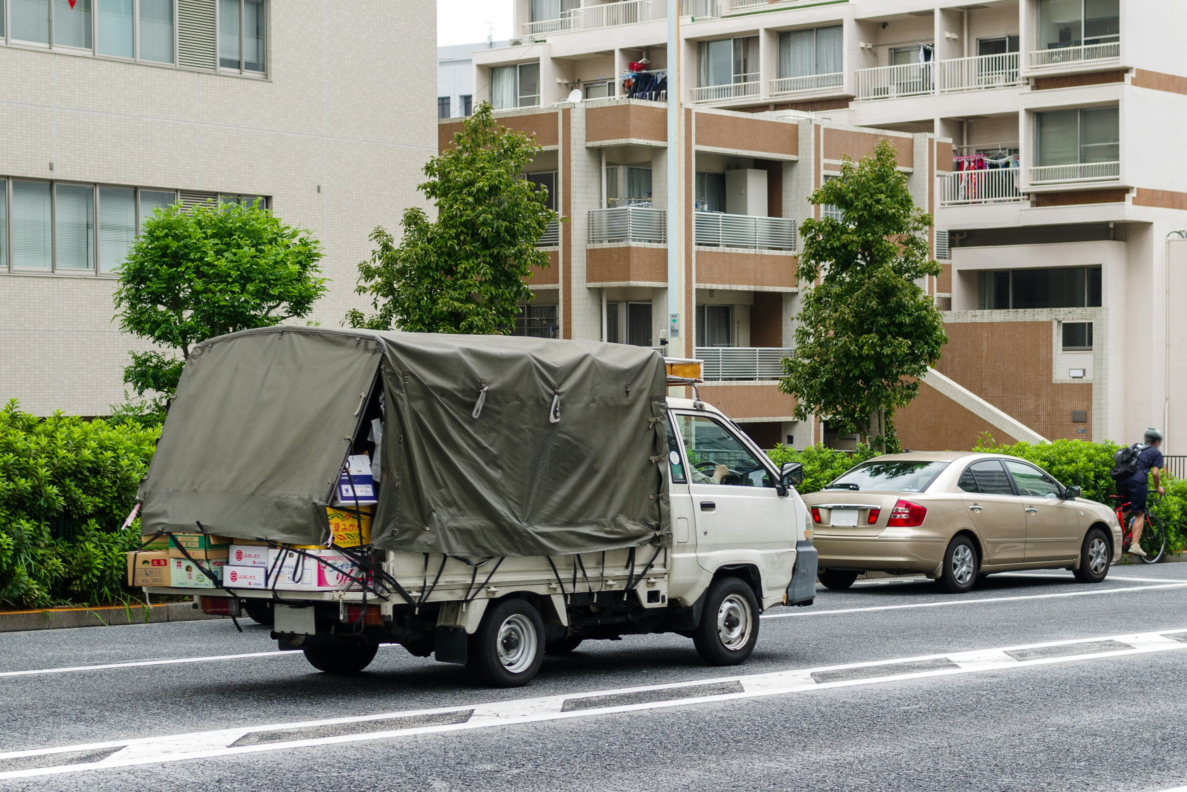 Olive green truck driving on a street with apartment buildings