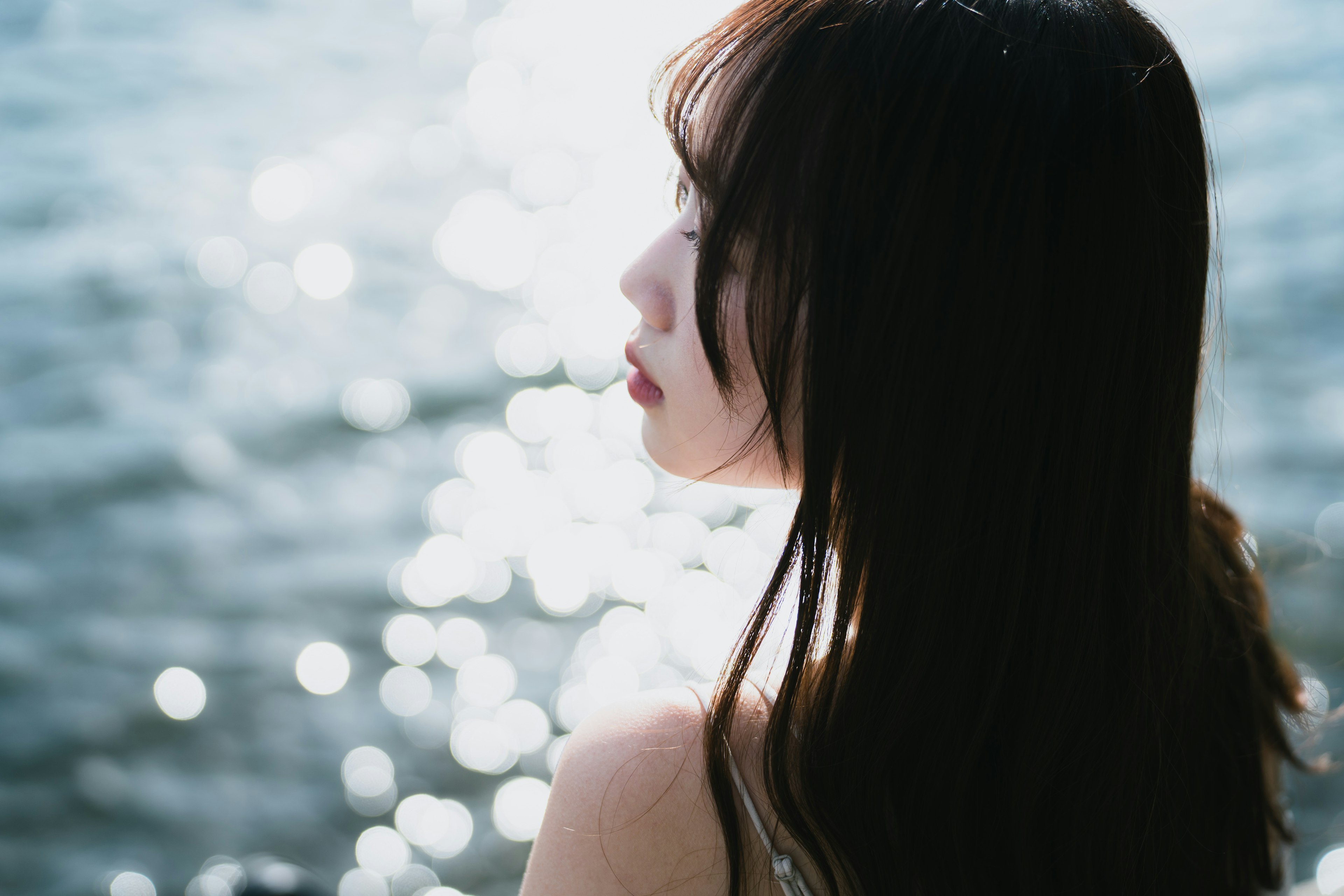 Seitenansicht einer Frau, die auf das Wasser schaut, mit verschwommenen Reflexionen im Hintergrund