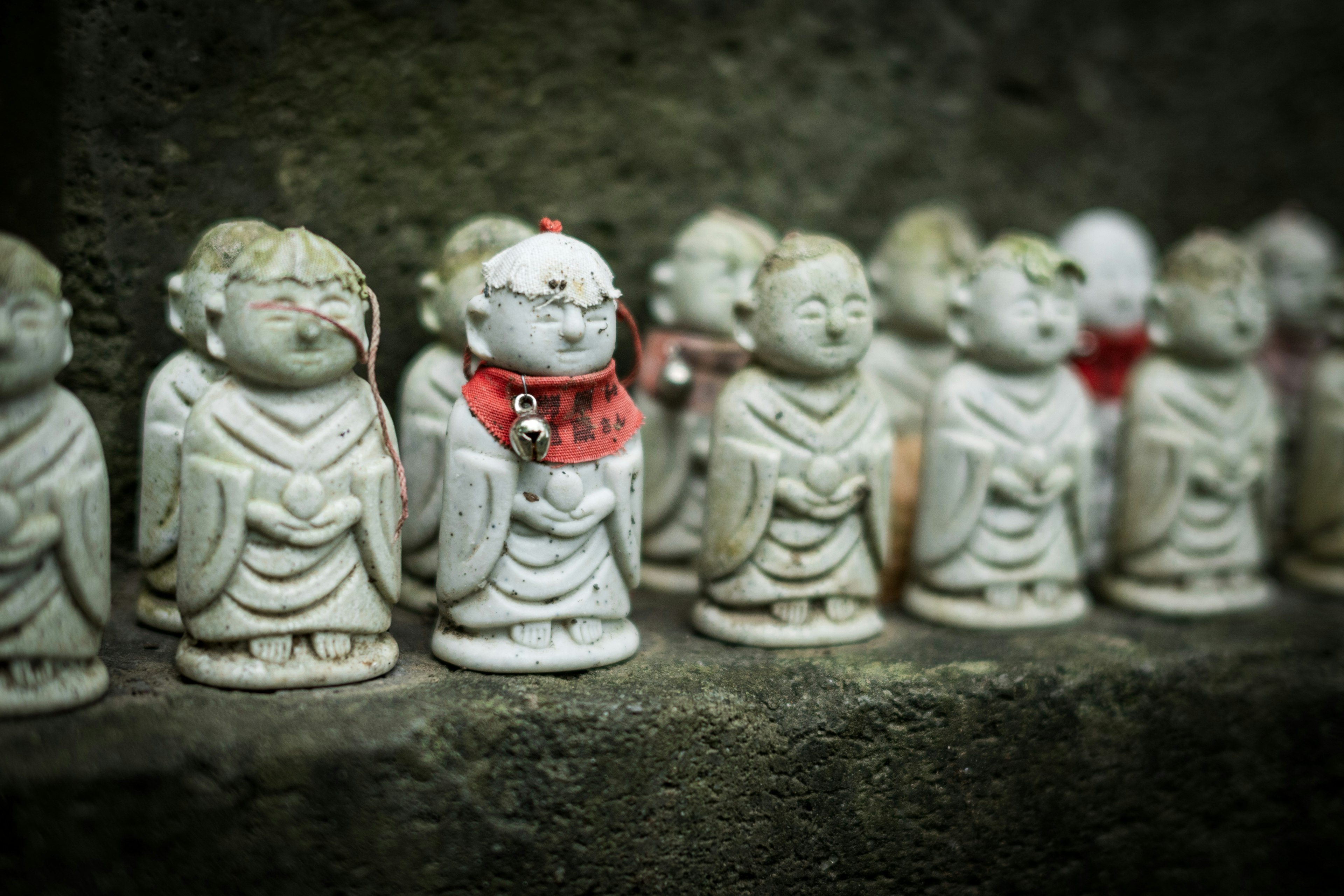 Small white statues of Buddhist figures lined up wearing red cloth