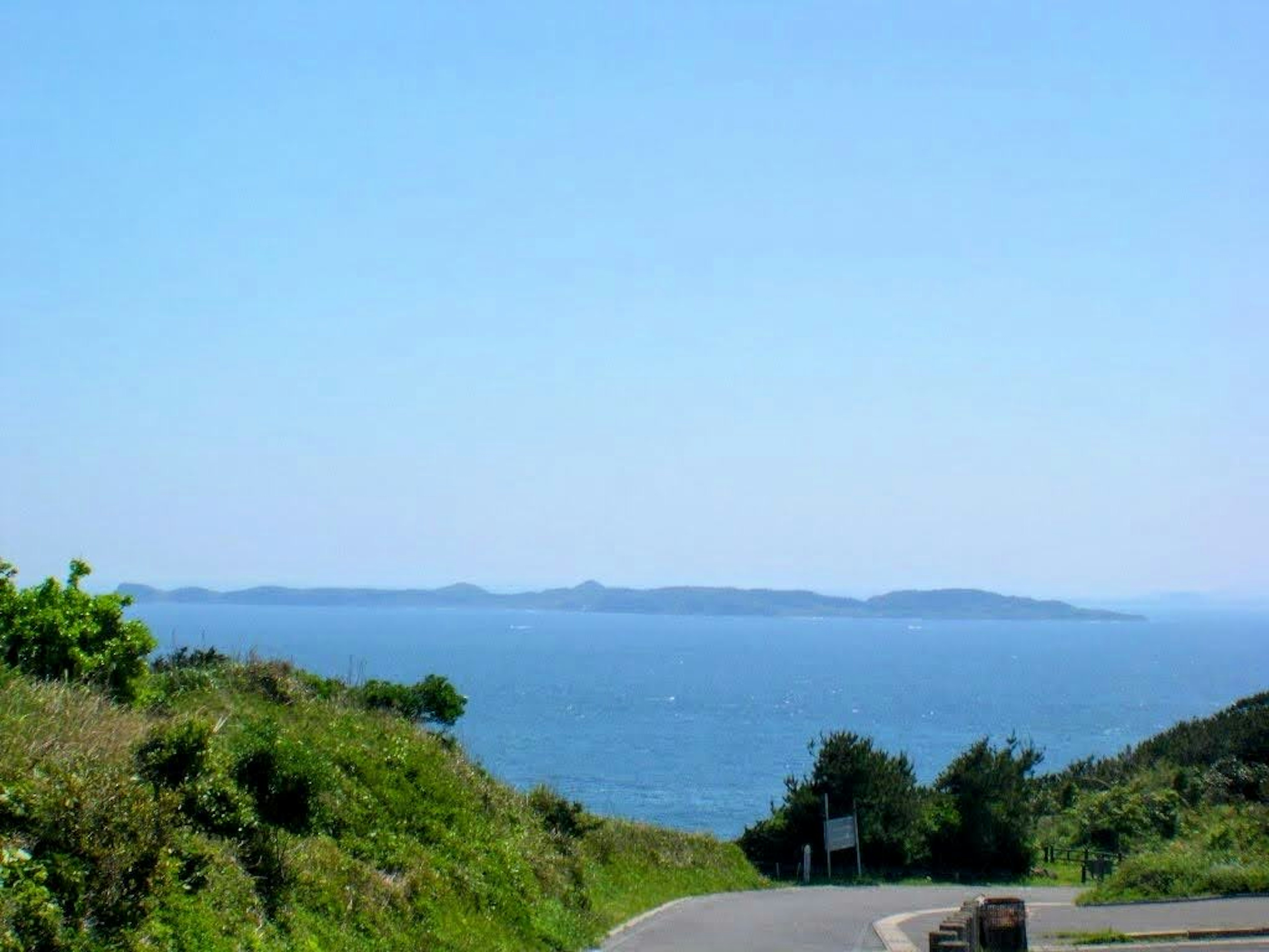 青い海と空の風景が広がる緑の丘の道