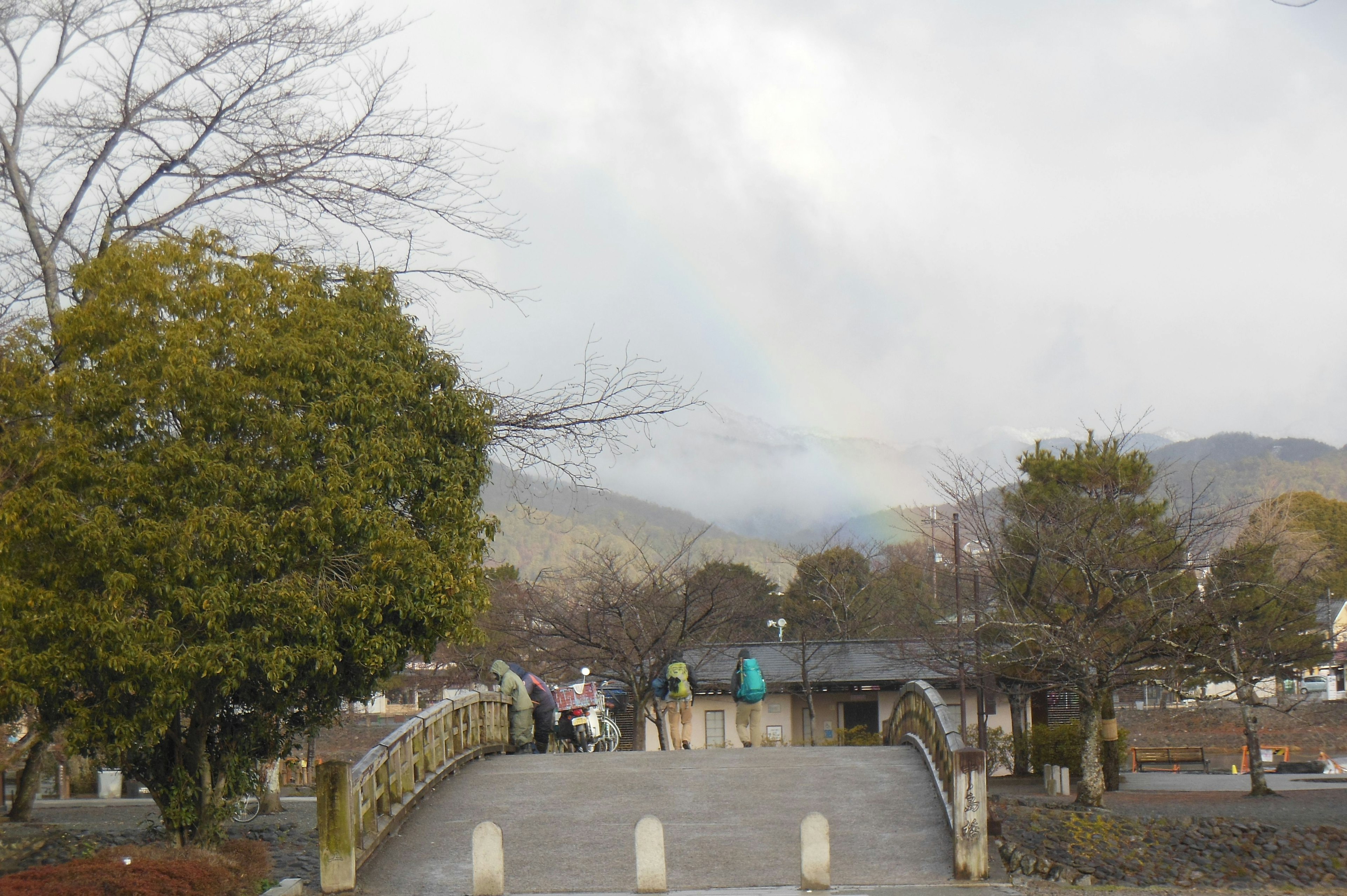 虹がかかる山々を背景にした橋と木々の景色