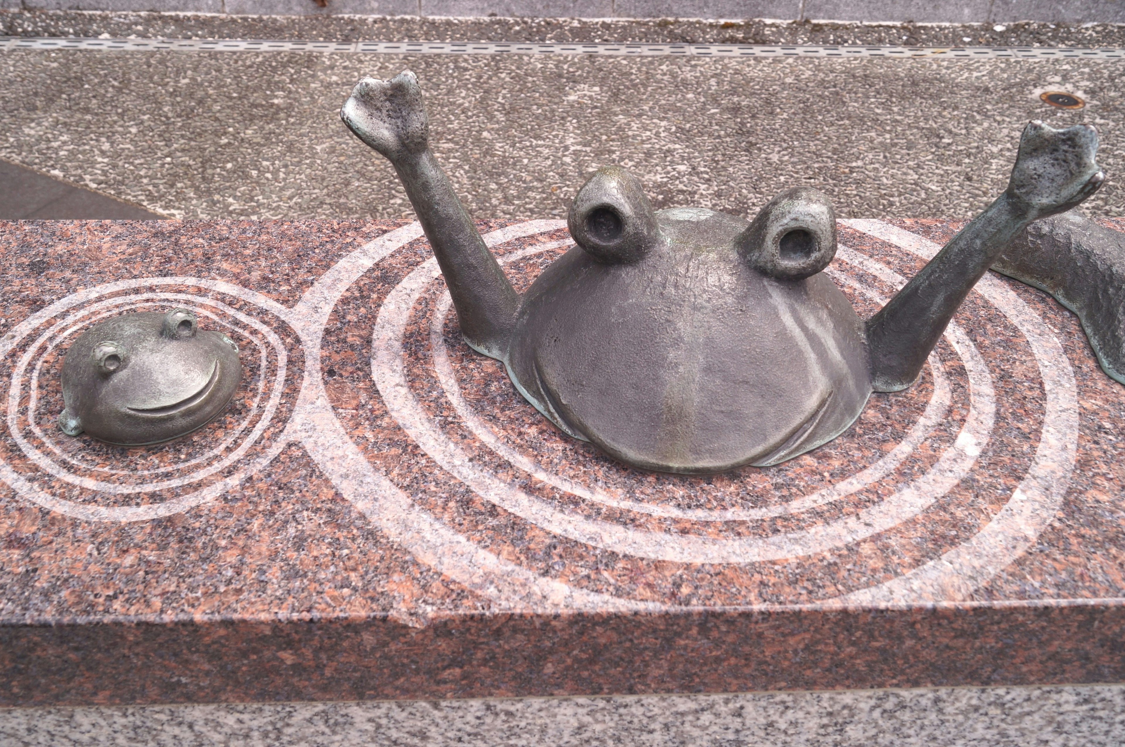 Sculptures de grenouilles créant des ondulations sur un banc en pierre