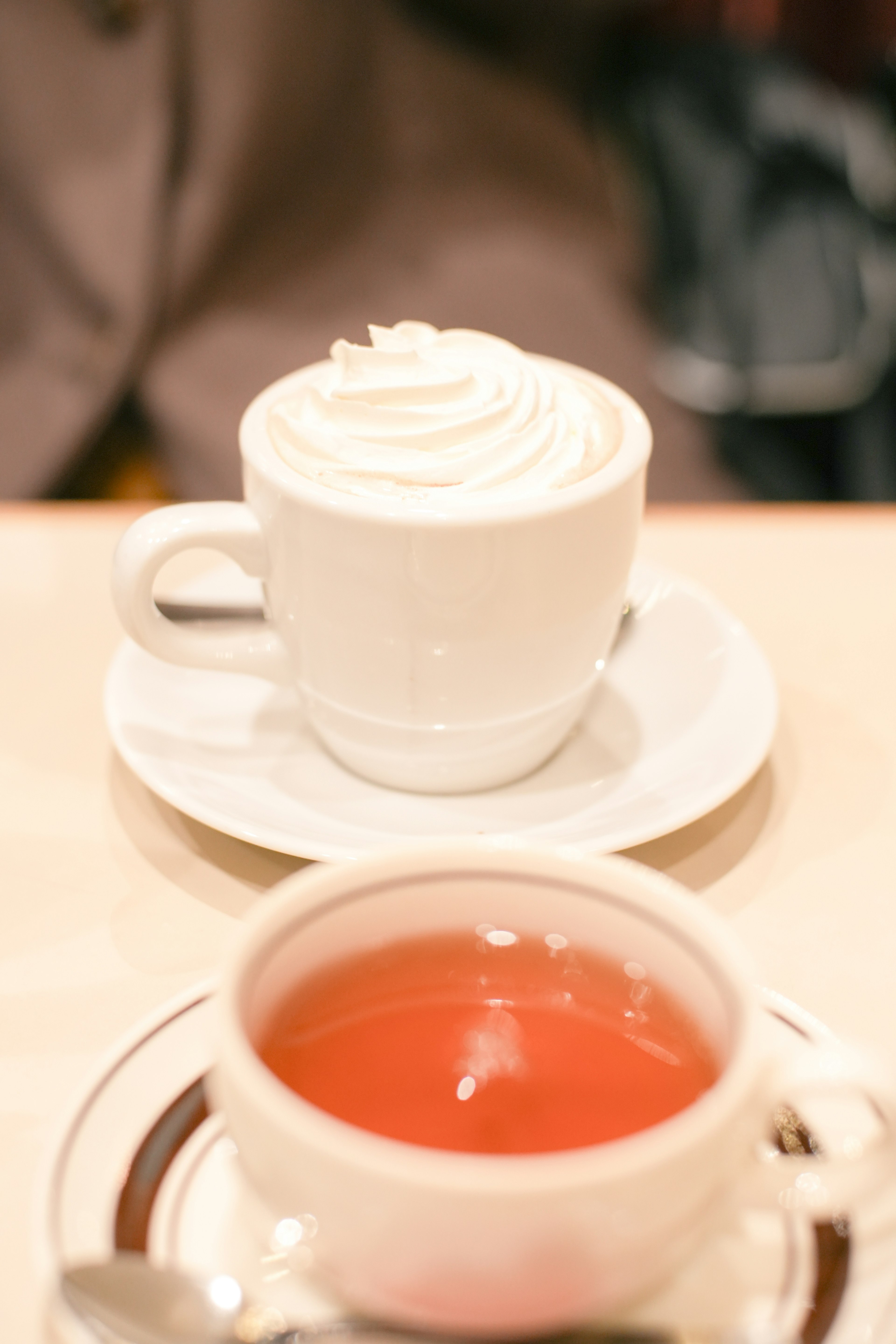 白いカップにクリームのトッピングがあるコーヒーと赤い紅茶が見える