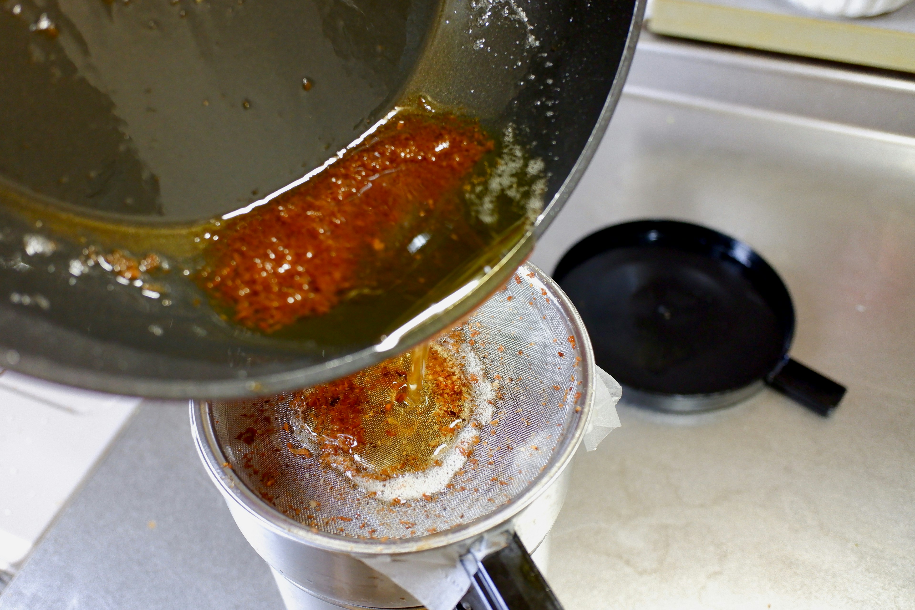 Versamento di olio da una padella in un colino