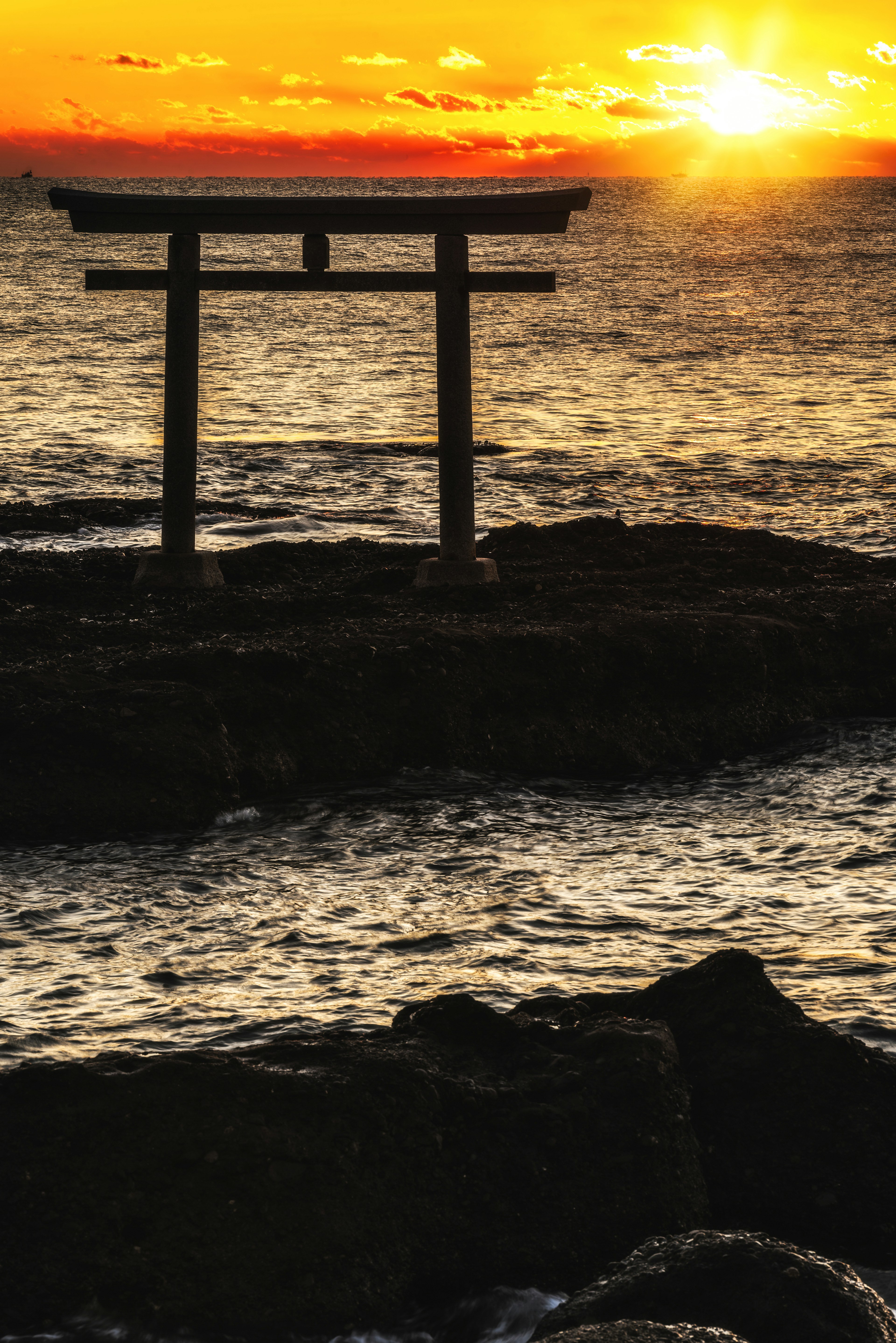 海岸に立つ鳥居と夕日のシルエット