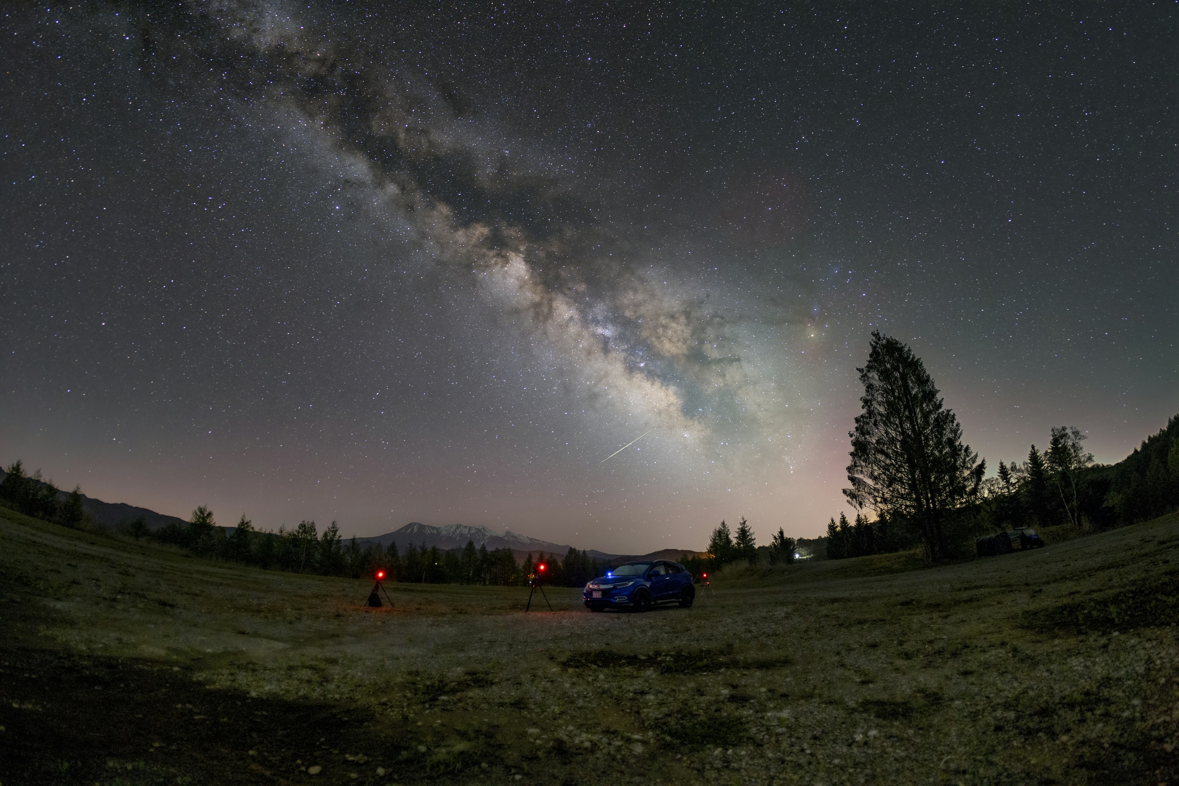 Vista mozzafiato della Via Lattea e delle stelle di notte con una macchina blu e alberi