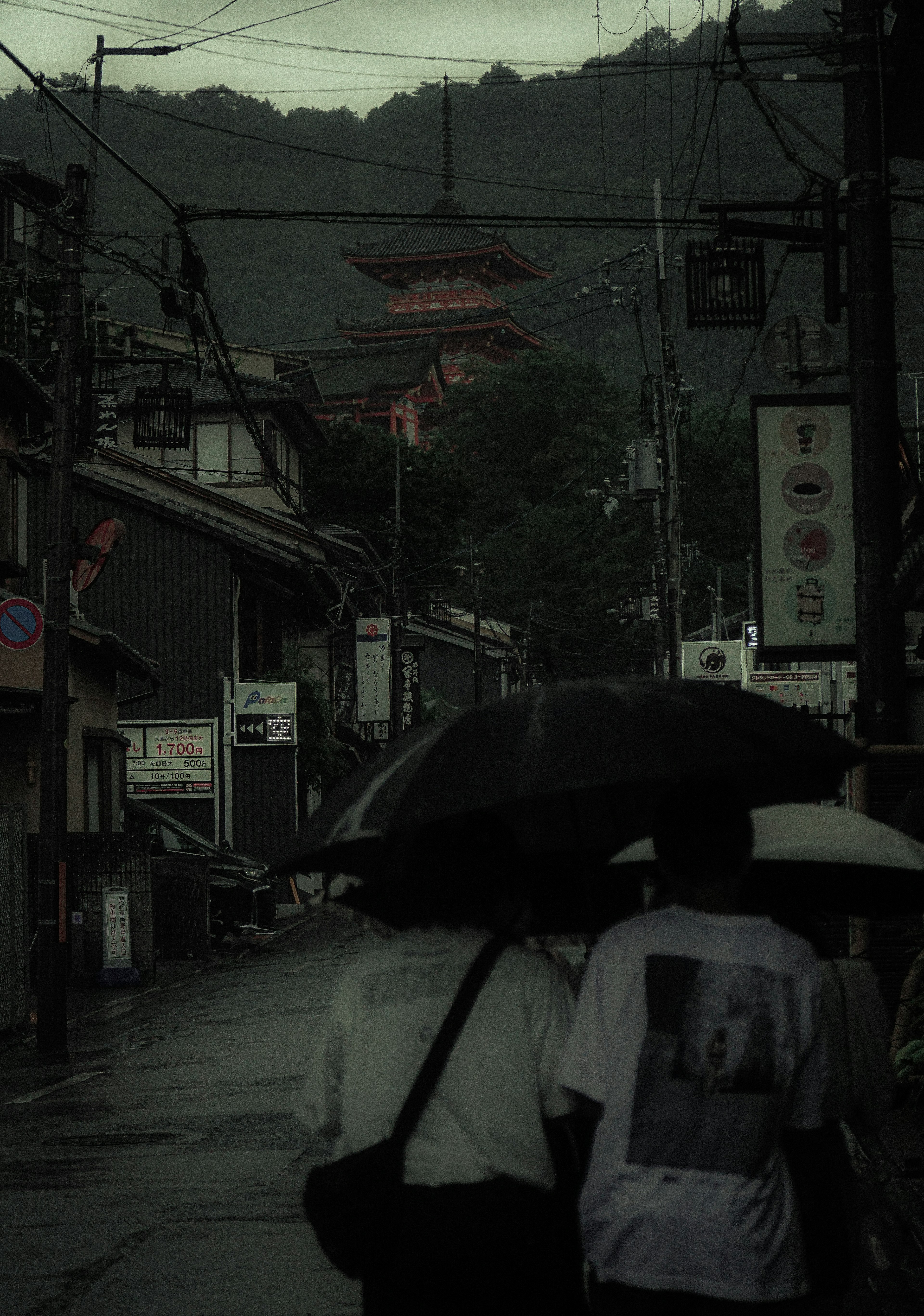 雨の日の静かな街並みで傘を差す二人の後ろ姿と山の中に見える寺のシルエット