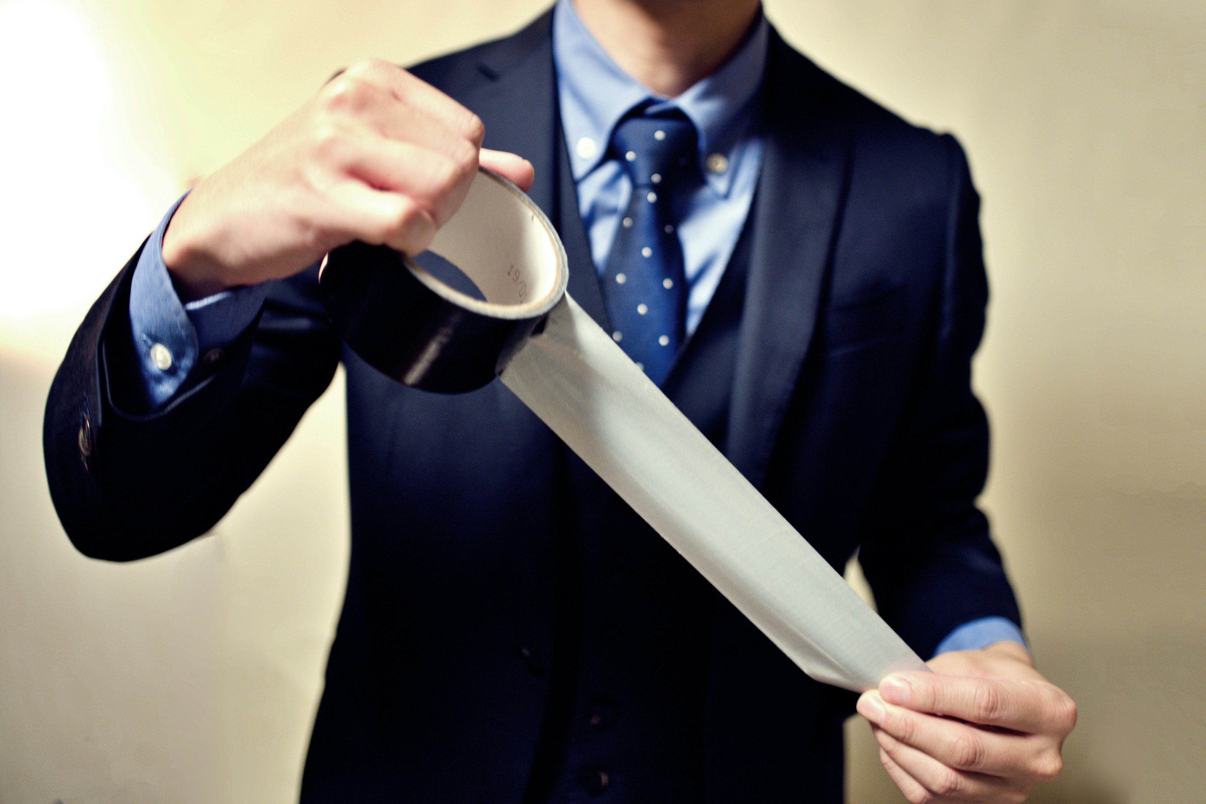 A man in a suit pulling clear tape from a roll