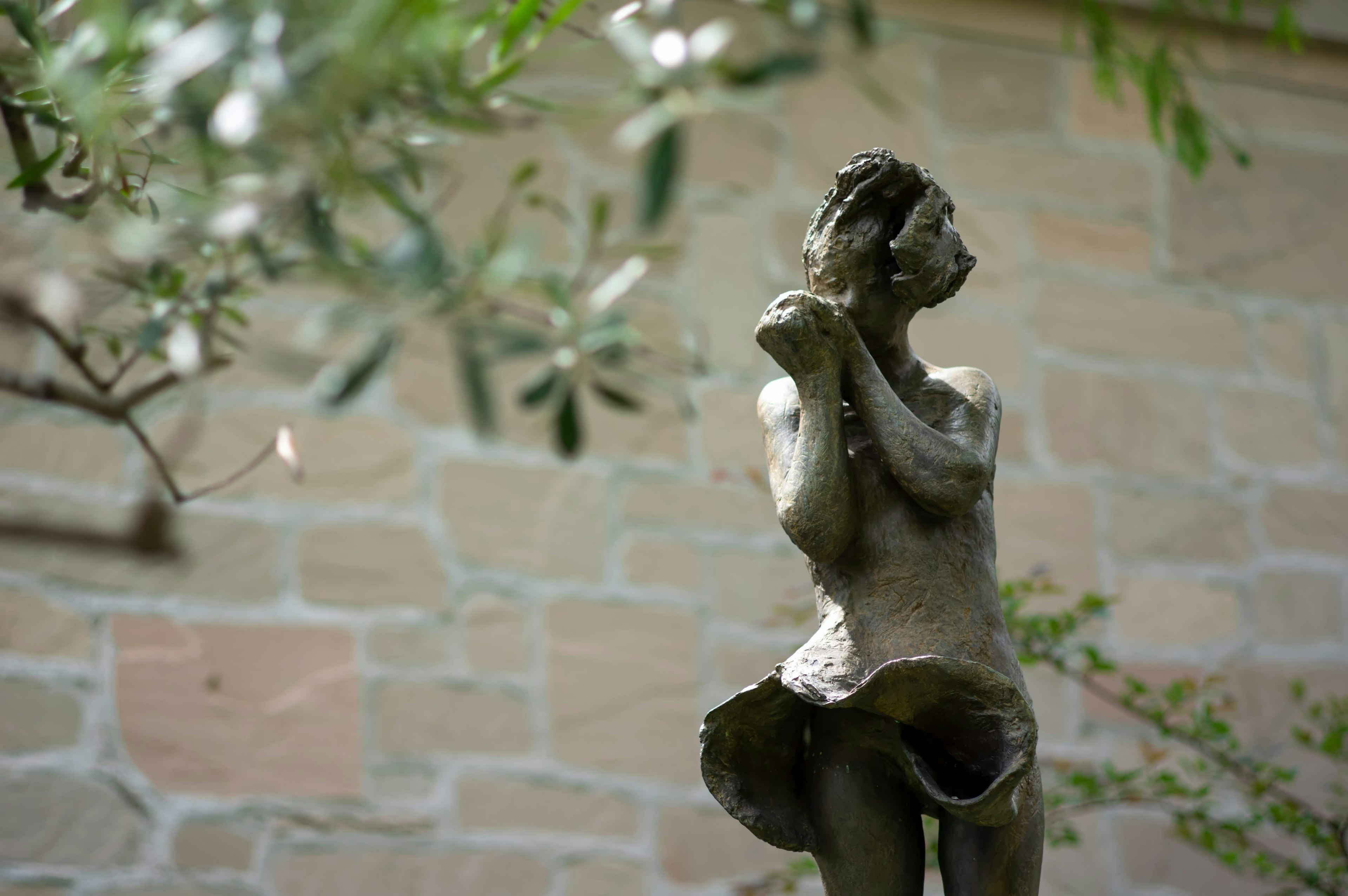 A female sculpture stands in a garden against a stone wall background