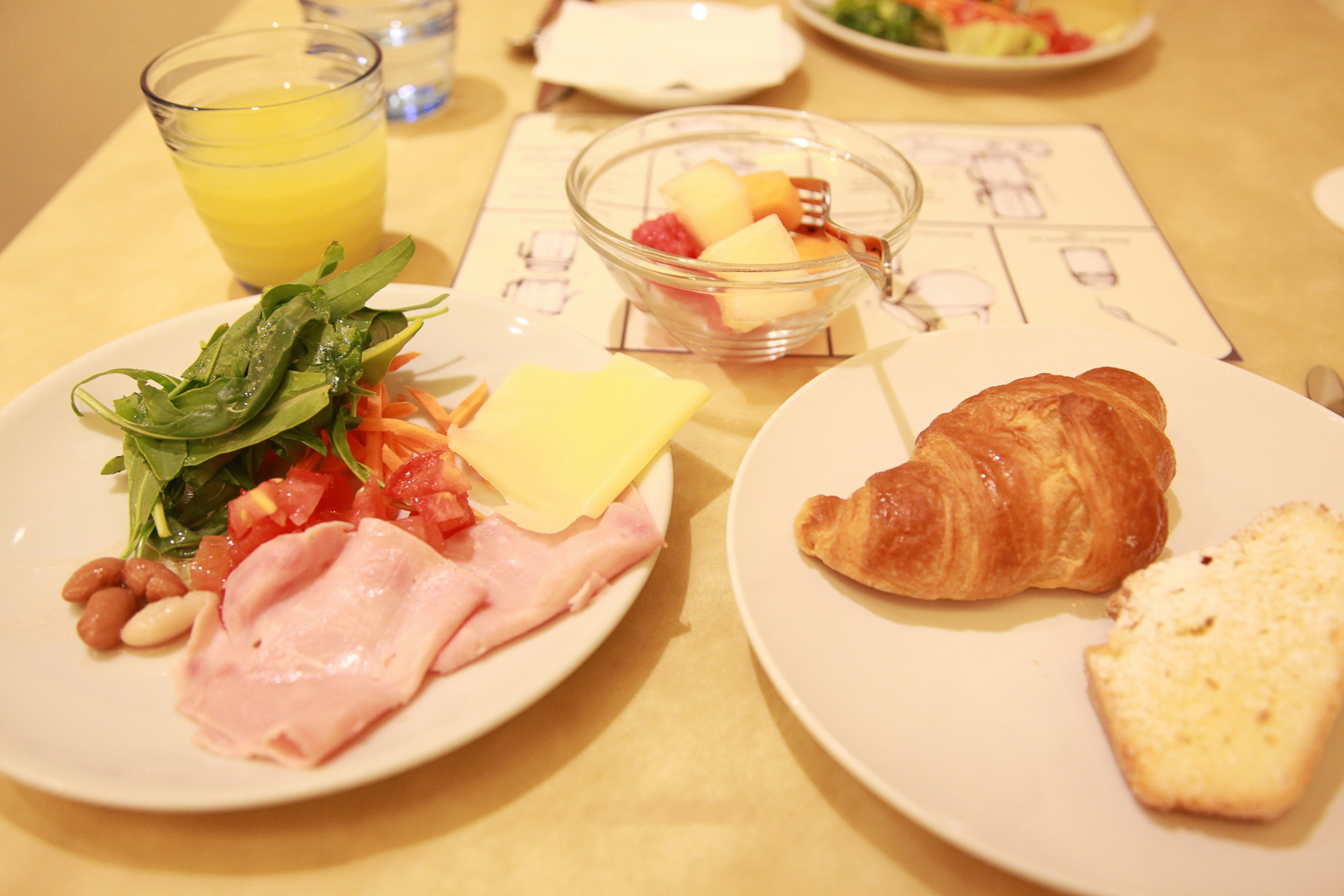 Plato de desayuno con ensalada fresca, jamón, queso, croissant y postre de frutas