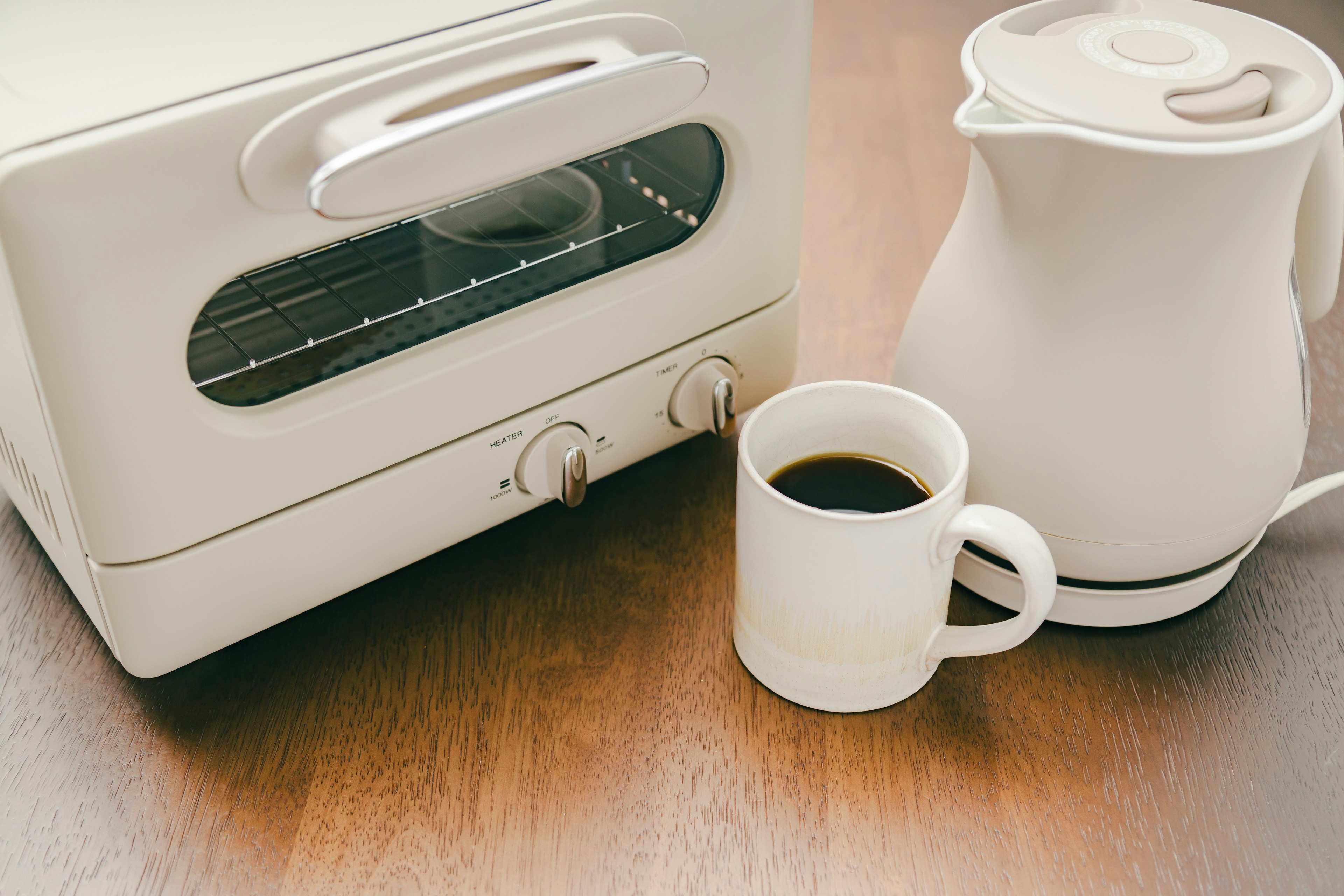 Ein weißer Toaster und ein Wasserkocher mit einer Tasse Kaffee auf einem Holztisch