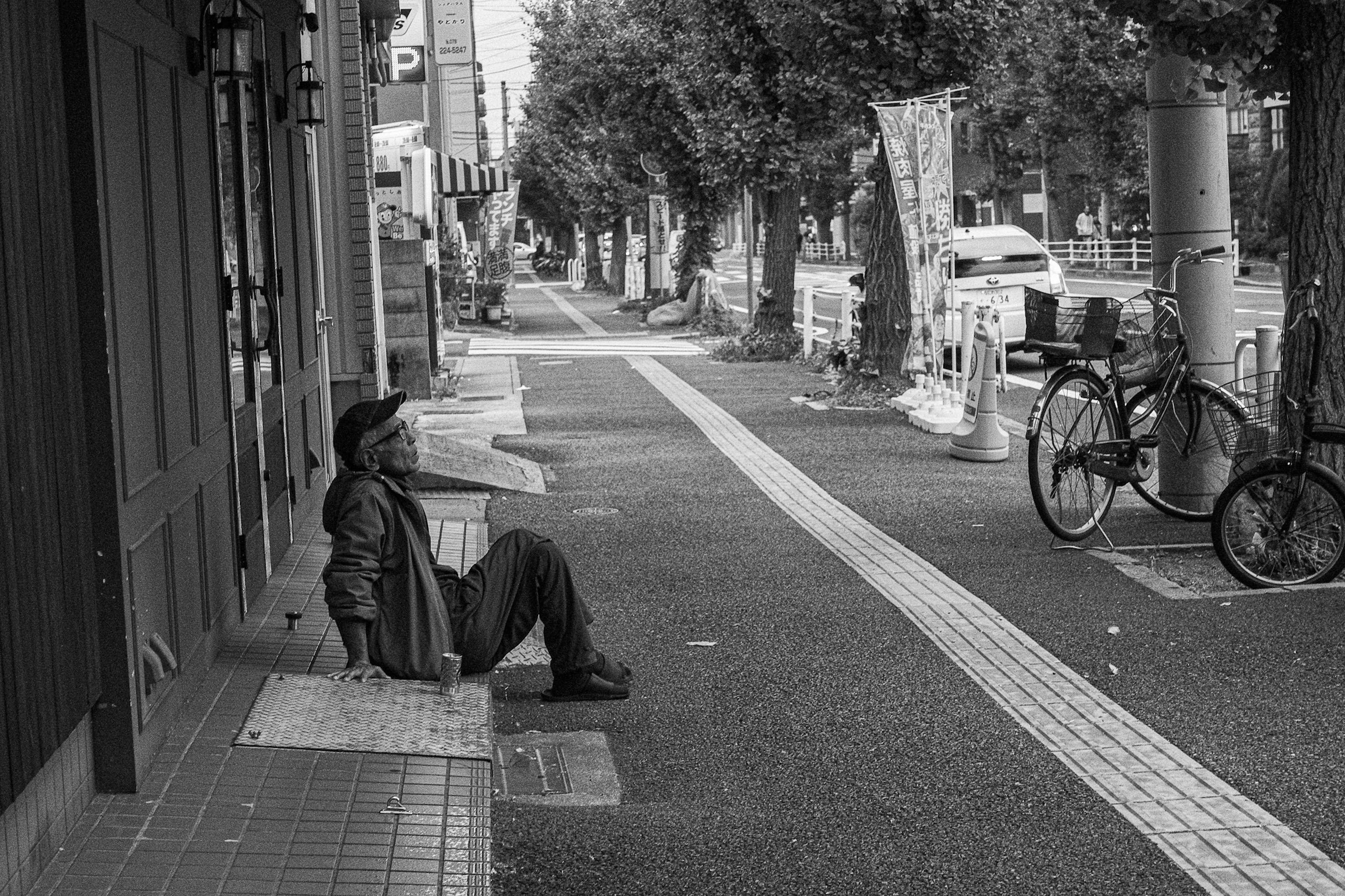 A man sitting on a sidewalk in a black and white street scene with a bicycle