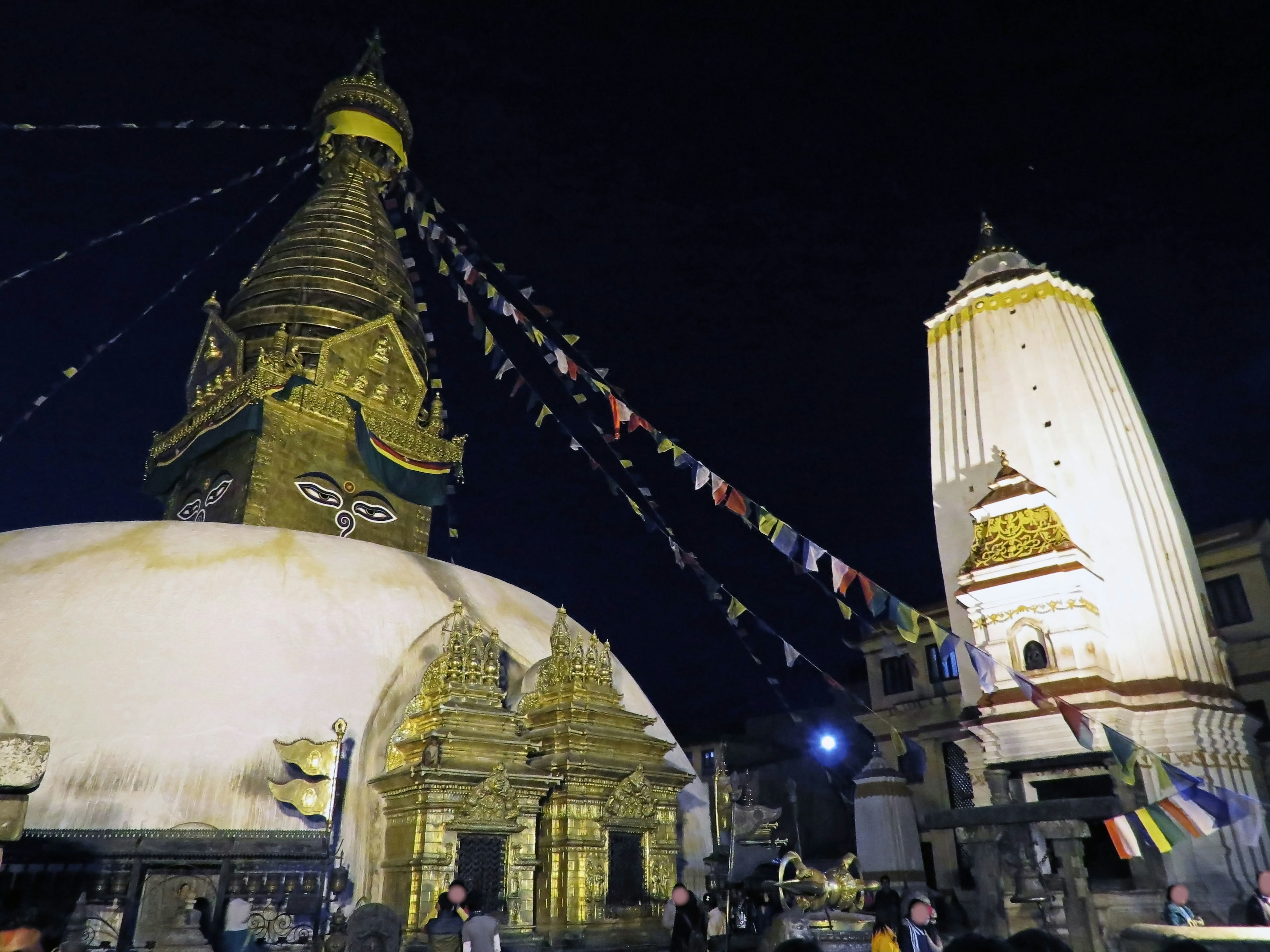 Nachtansicht der Boudhanath-Stupa mit Gebetsfahnen und angrenzendem Tempel