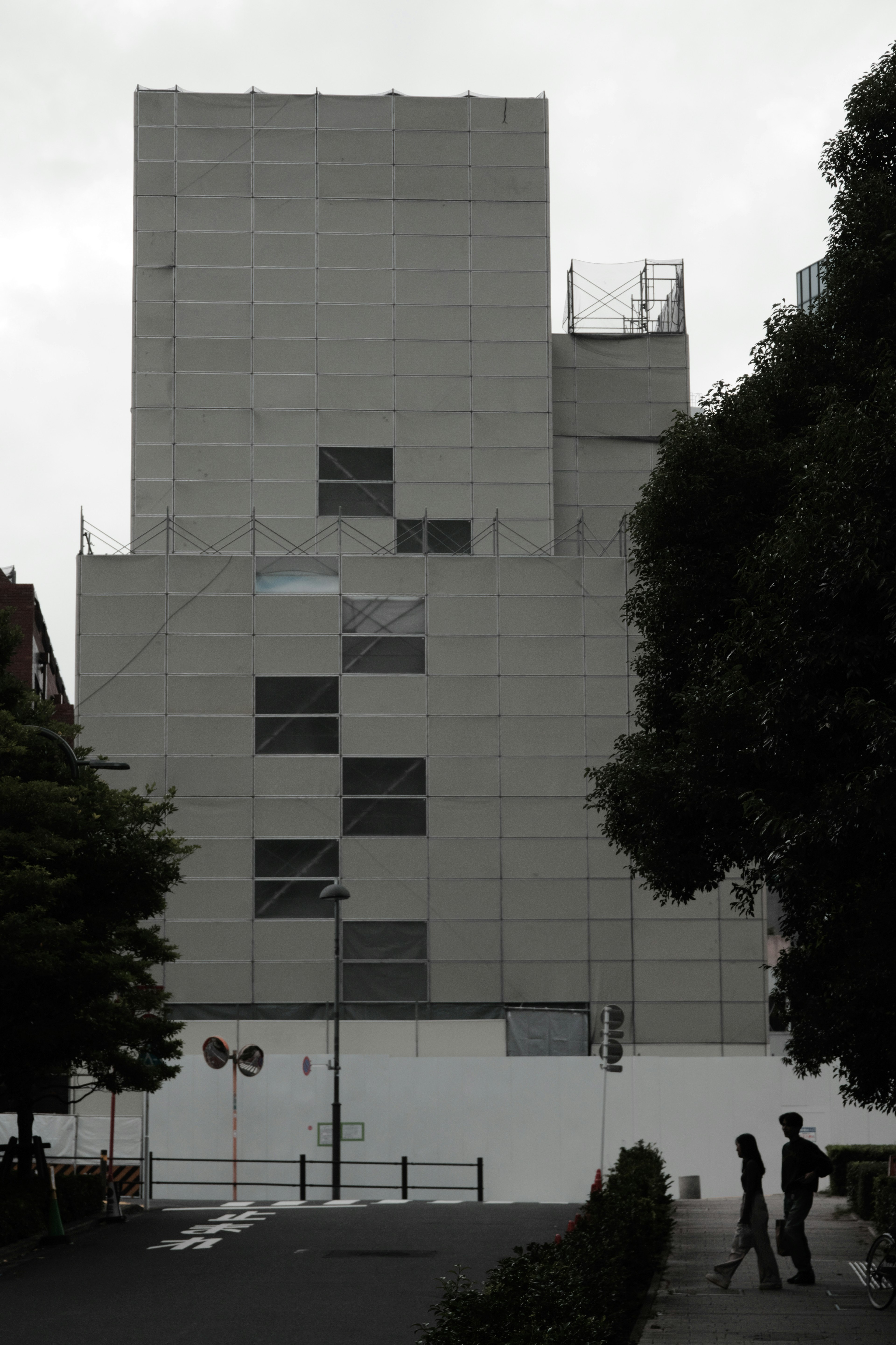 Gray modern building with surrounding trees and pedestrians