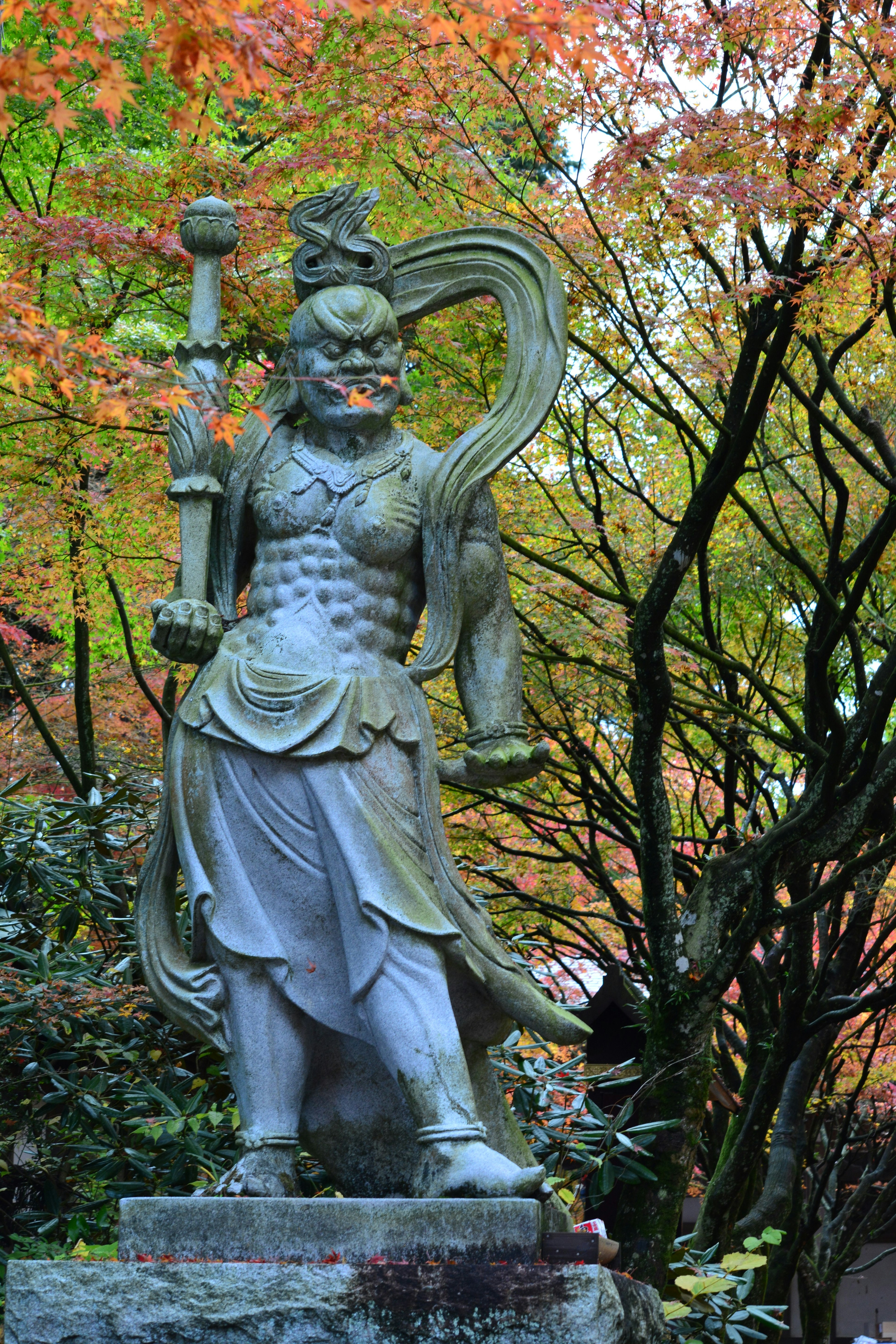 Una grande statua di guerriero in pietra circondata da foglie autunnali