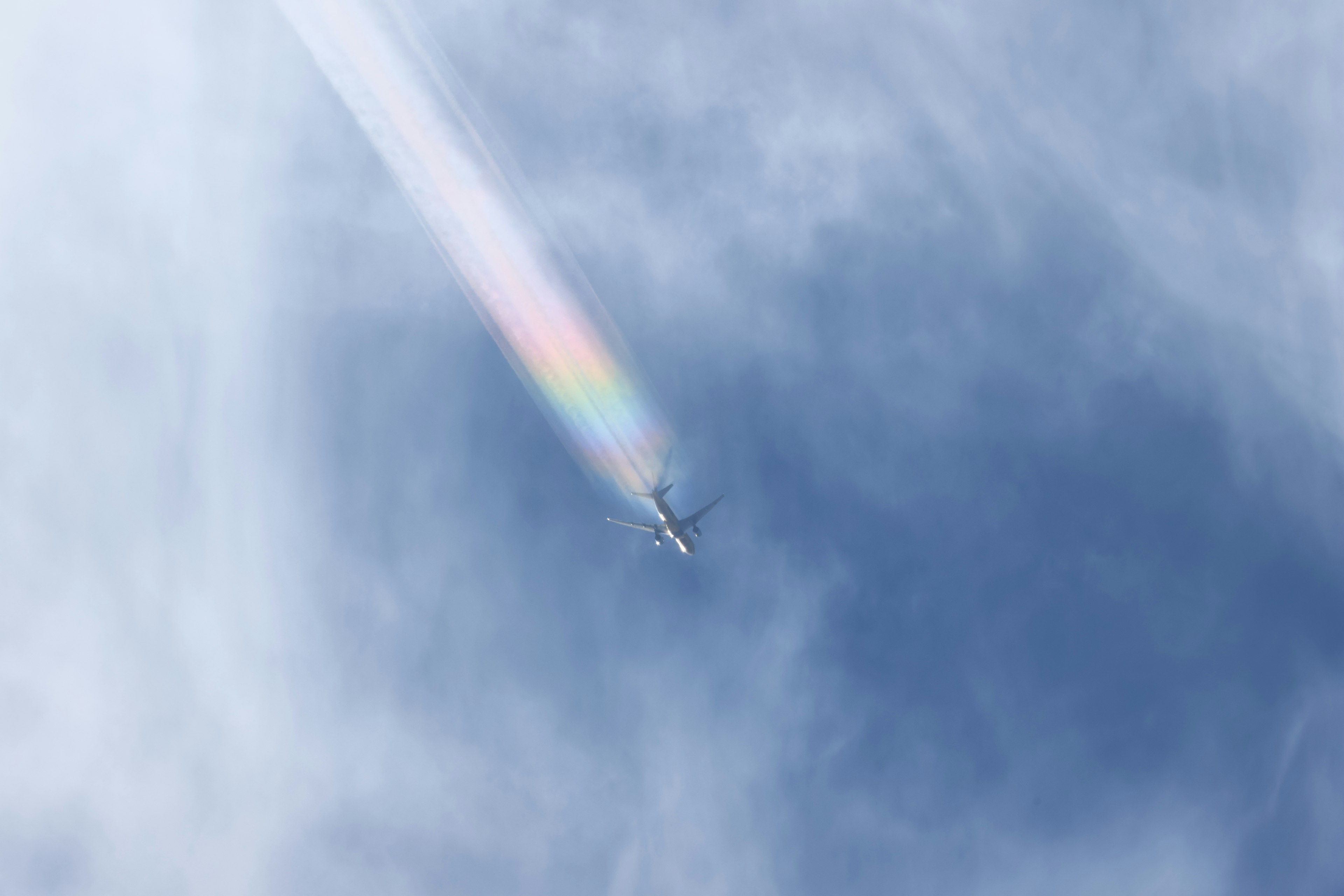 An airplane flying in a blue sky leaving a rainbow-colored trail