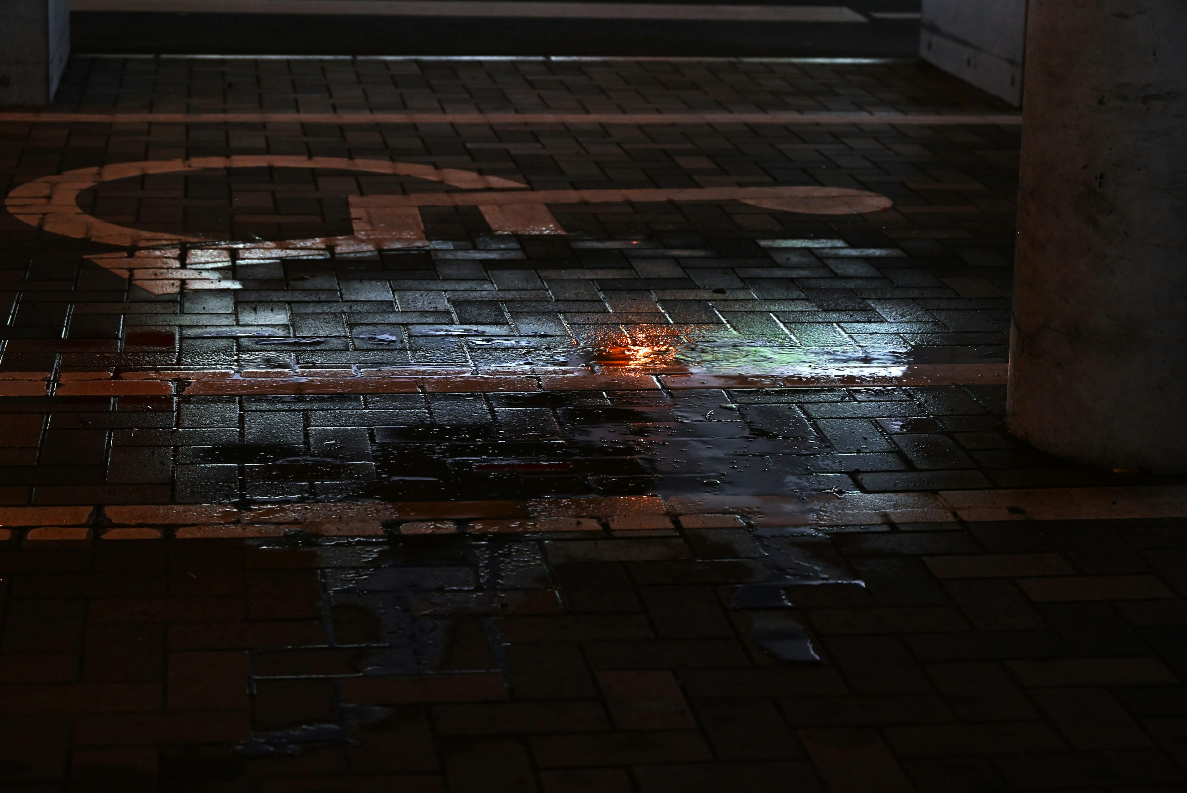 A dark environment with a wet tiled floor featuring a wheelchair symbol