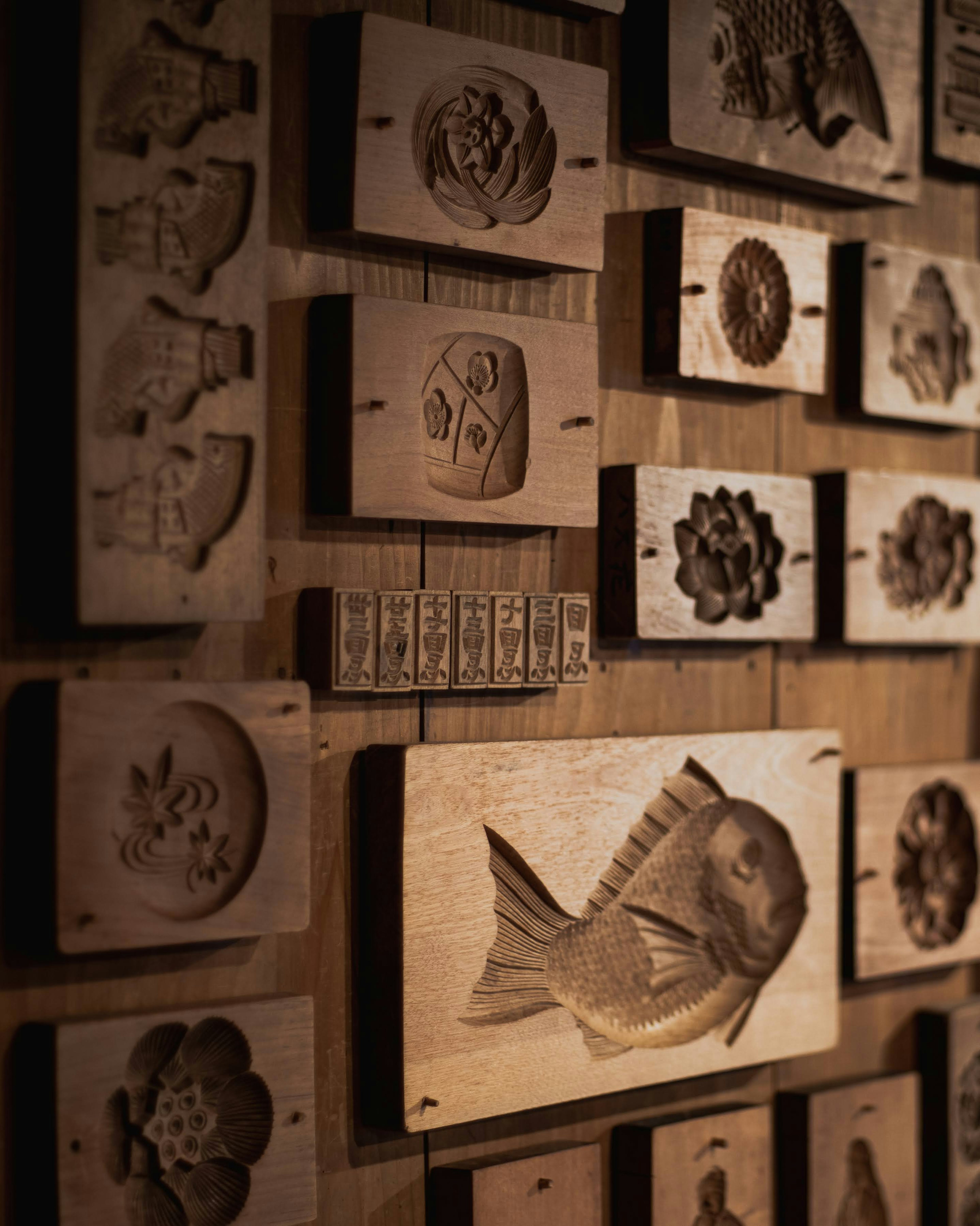 Wooden molds carved with fish and various patterns displayed on a wall